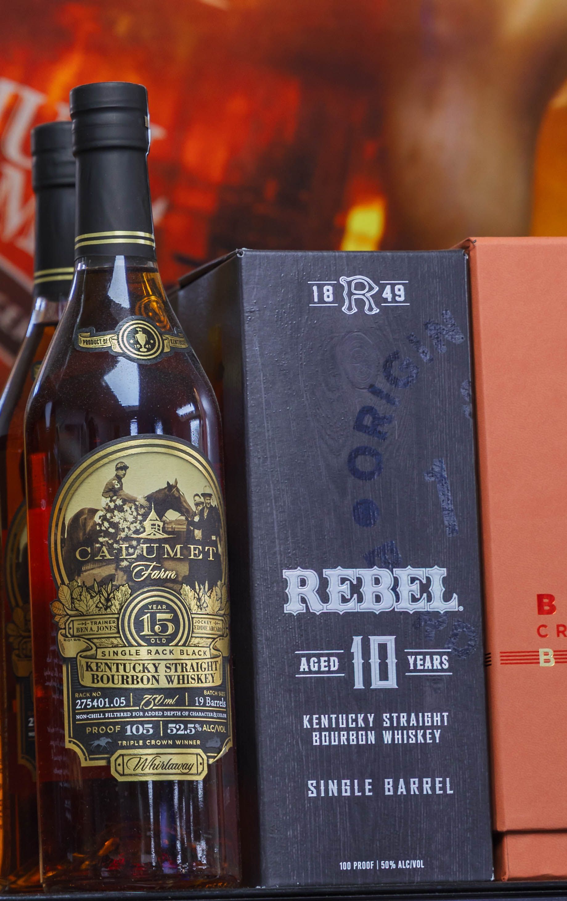 Bottles of Rebel 10-year Kentucky Straight Bourbon, with a dark box, in front of an orange background.