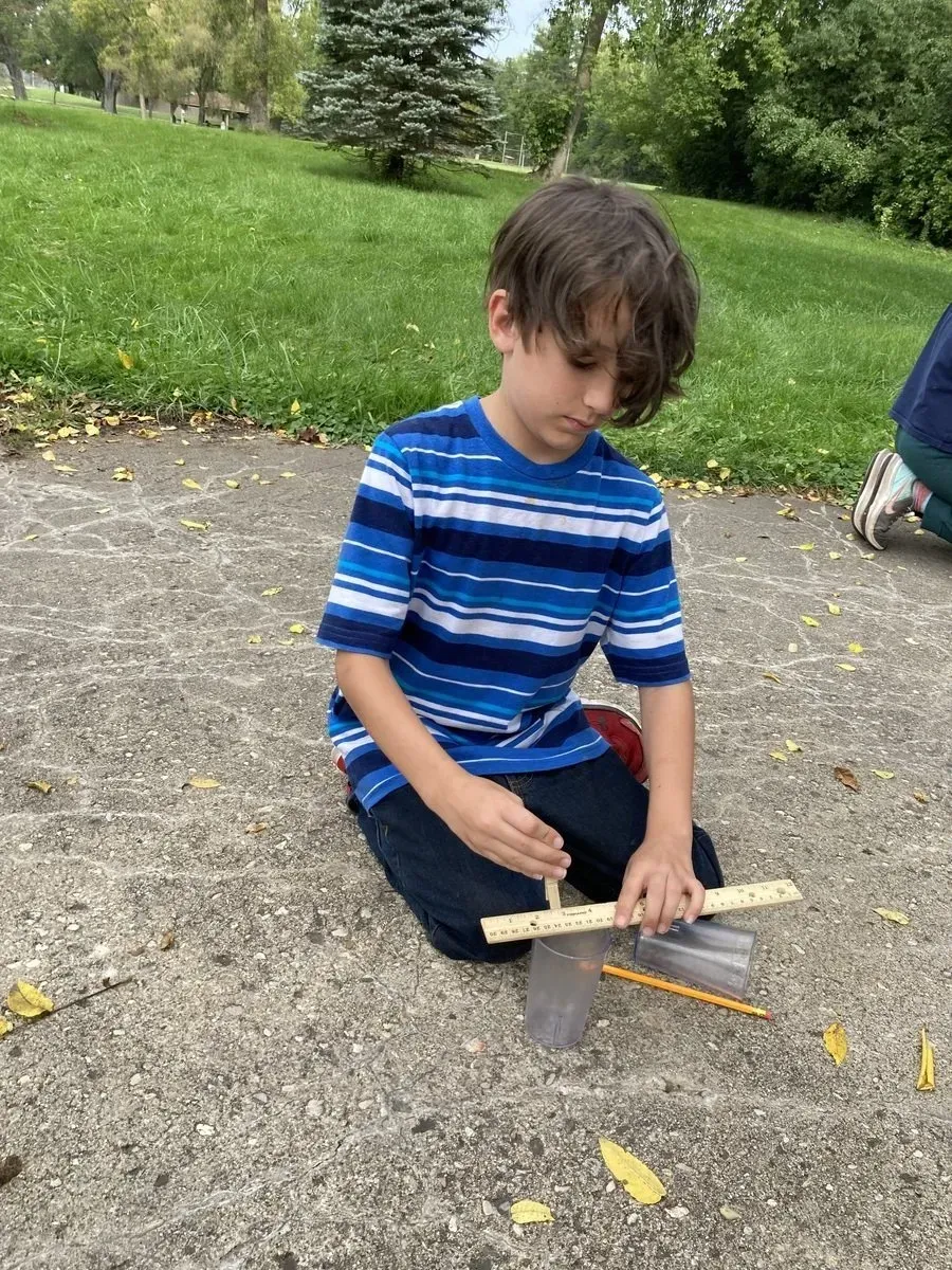 a young boy is kneeling on the ground holding a ruler and a pencil