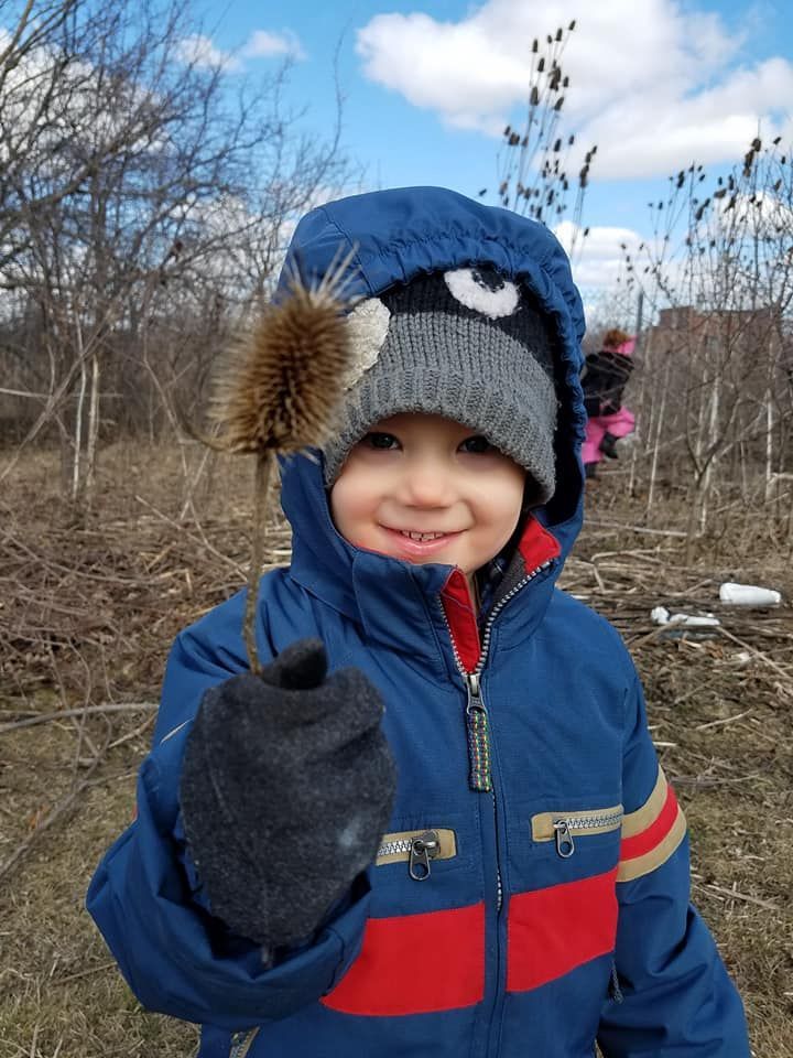 a young boy wearing a blue jacket and a hat is holding a bird in his hand
