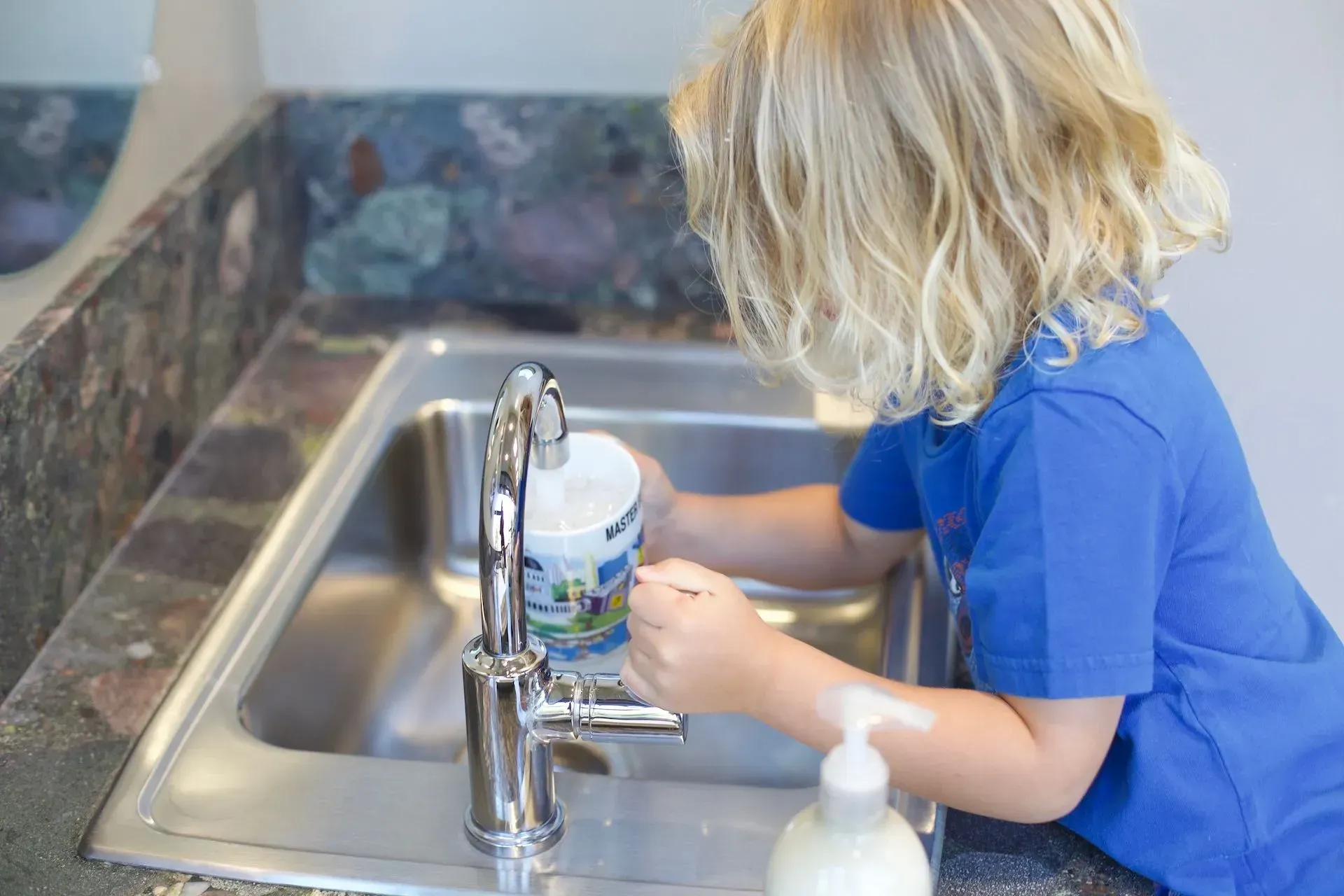 Montessori child is washing dishes in a kitchen sink.