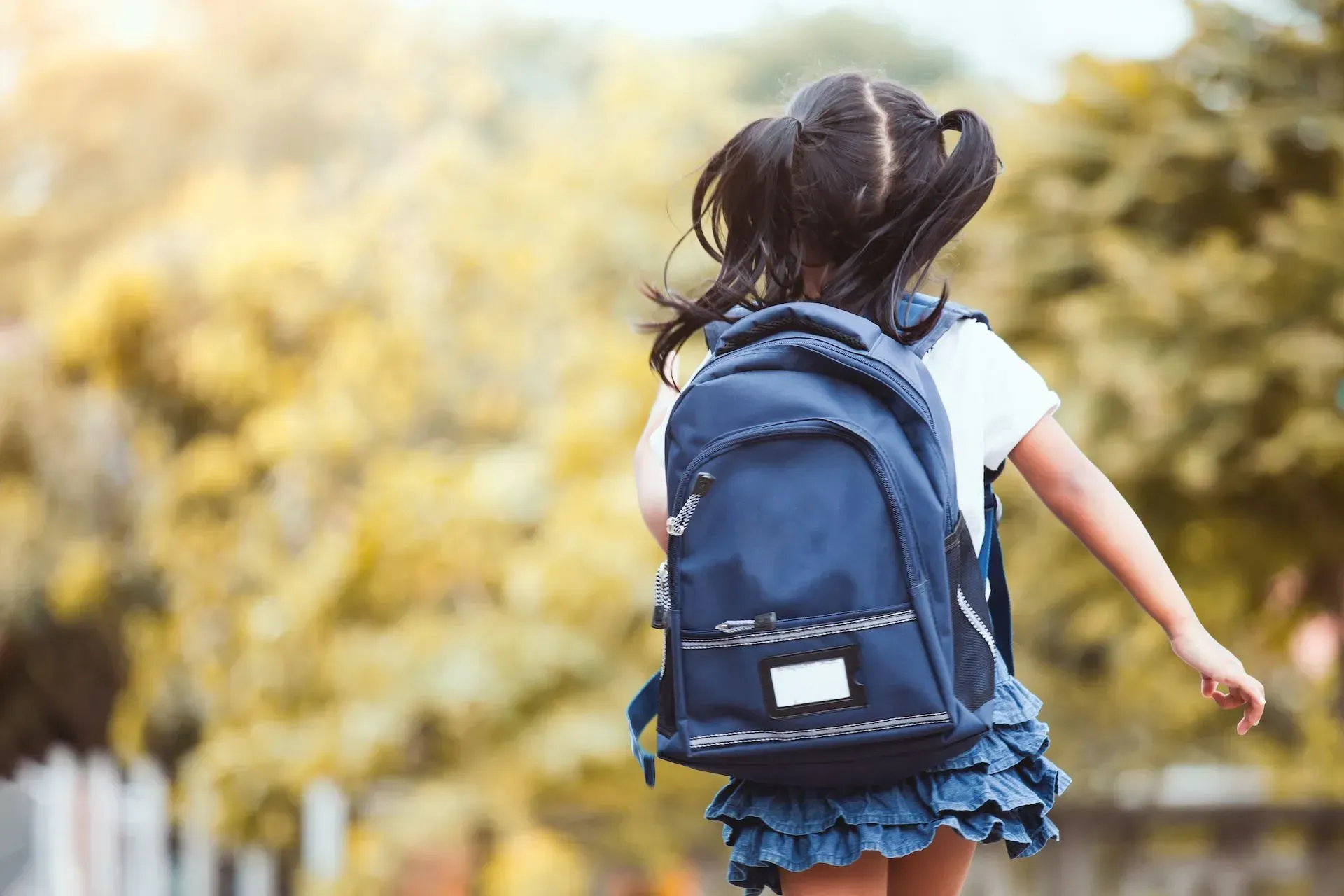 A little girl with a backpack is walking in the park.