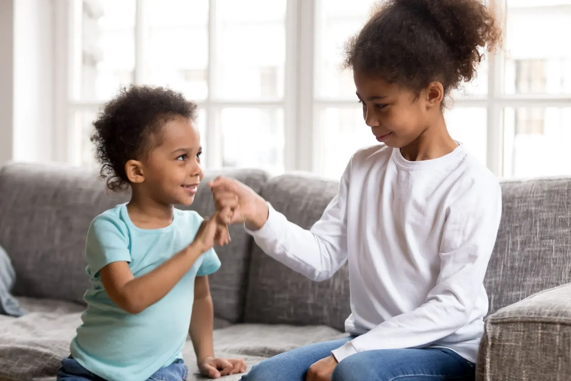 two young girls are sitting on a couch giving each other a high five .