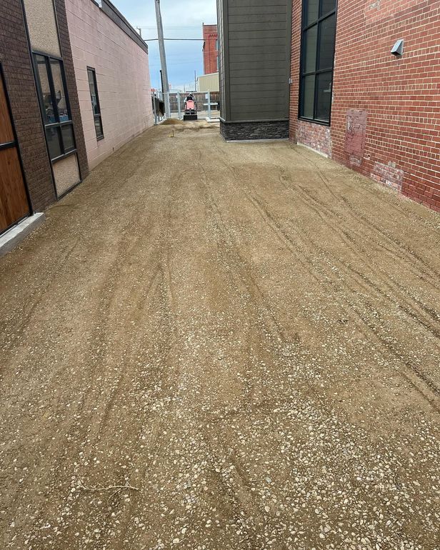A dirt road between two buildings with a brick building in the background.