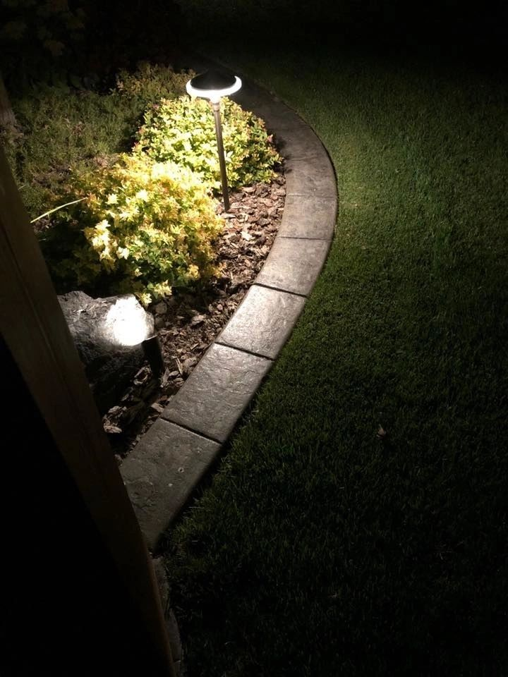 A lawn with a brick border and lights on it at night.