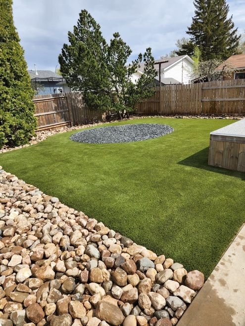 A backyard with a lush green lawn and rocks.
