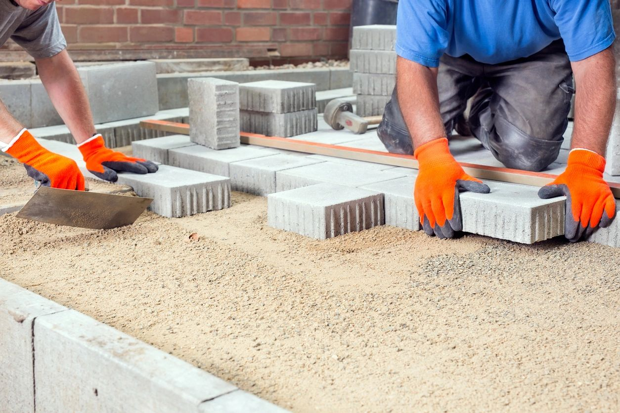 Two men are laying bricks on a sidewalk.