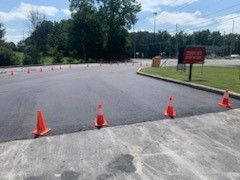 Orange traffic cones line a paved area next to a sign, possibly a driving test course.