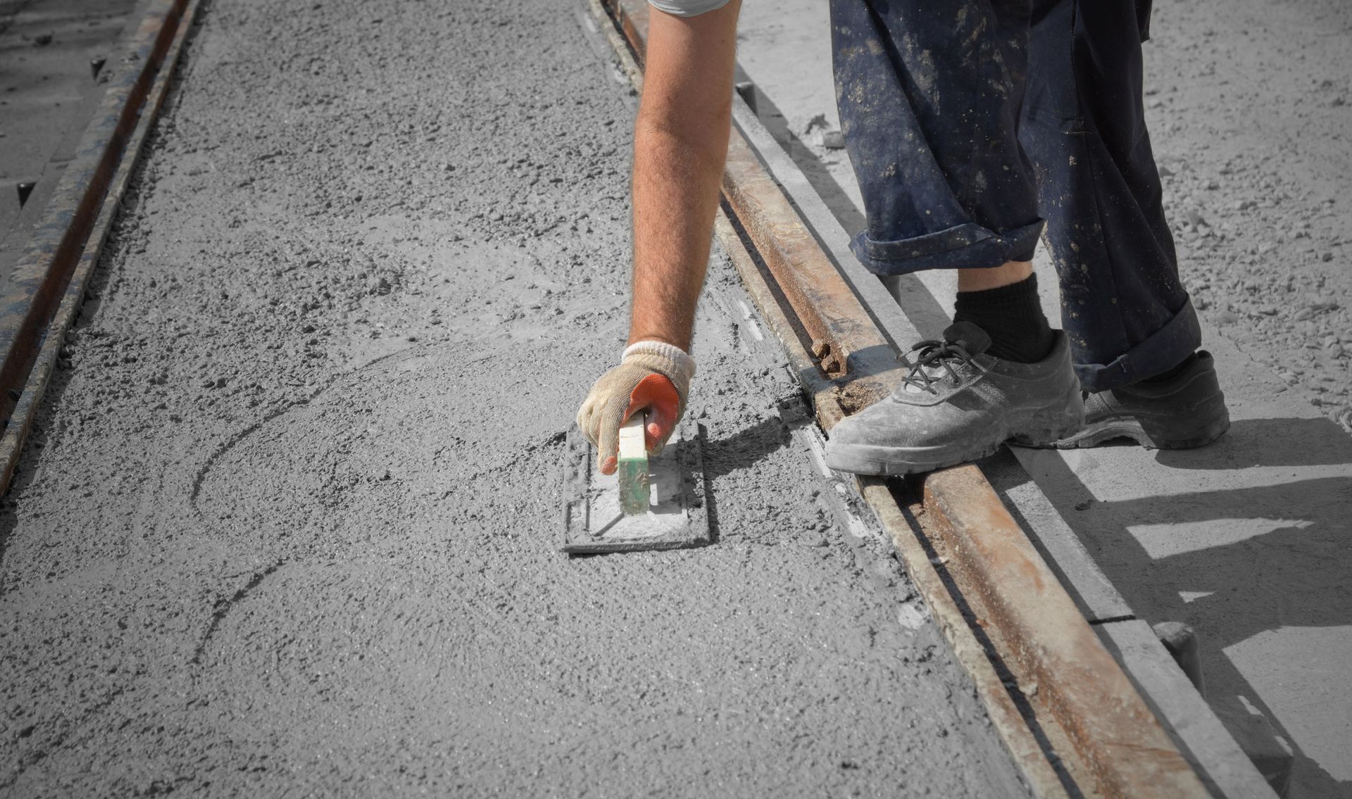 Worker smoothing wet concrete with a hand trowel on a construction site for quality finish prep task.