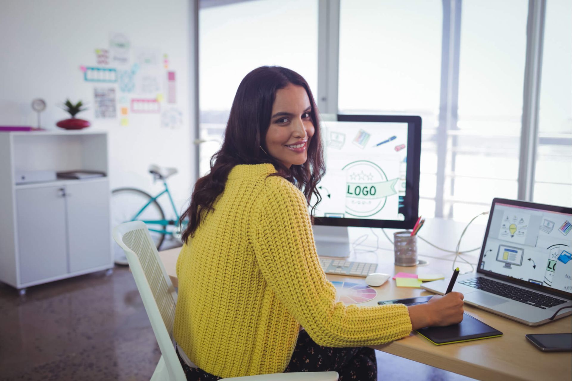 A woman is sitting at a desk with a computer and a laptop.