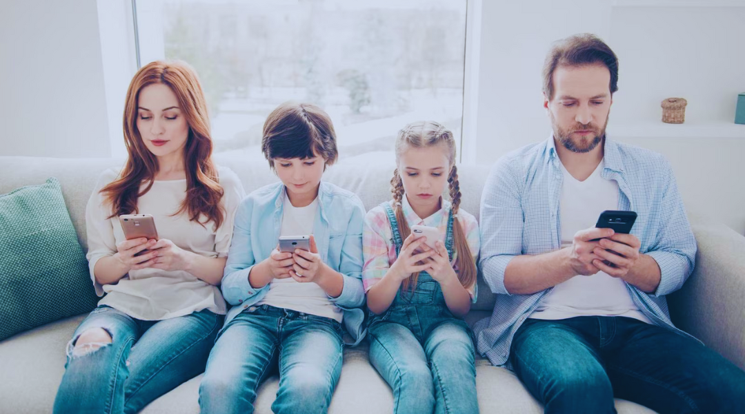 A family is sitting on a couch looking at their phones.