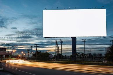 A large white billboard is sitting on the side of a road.