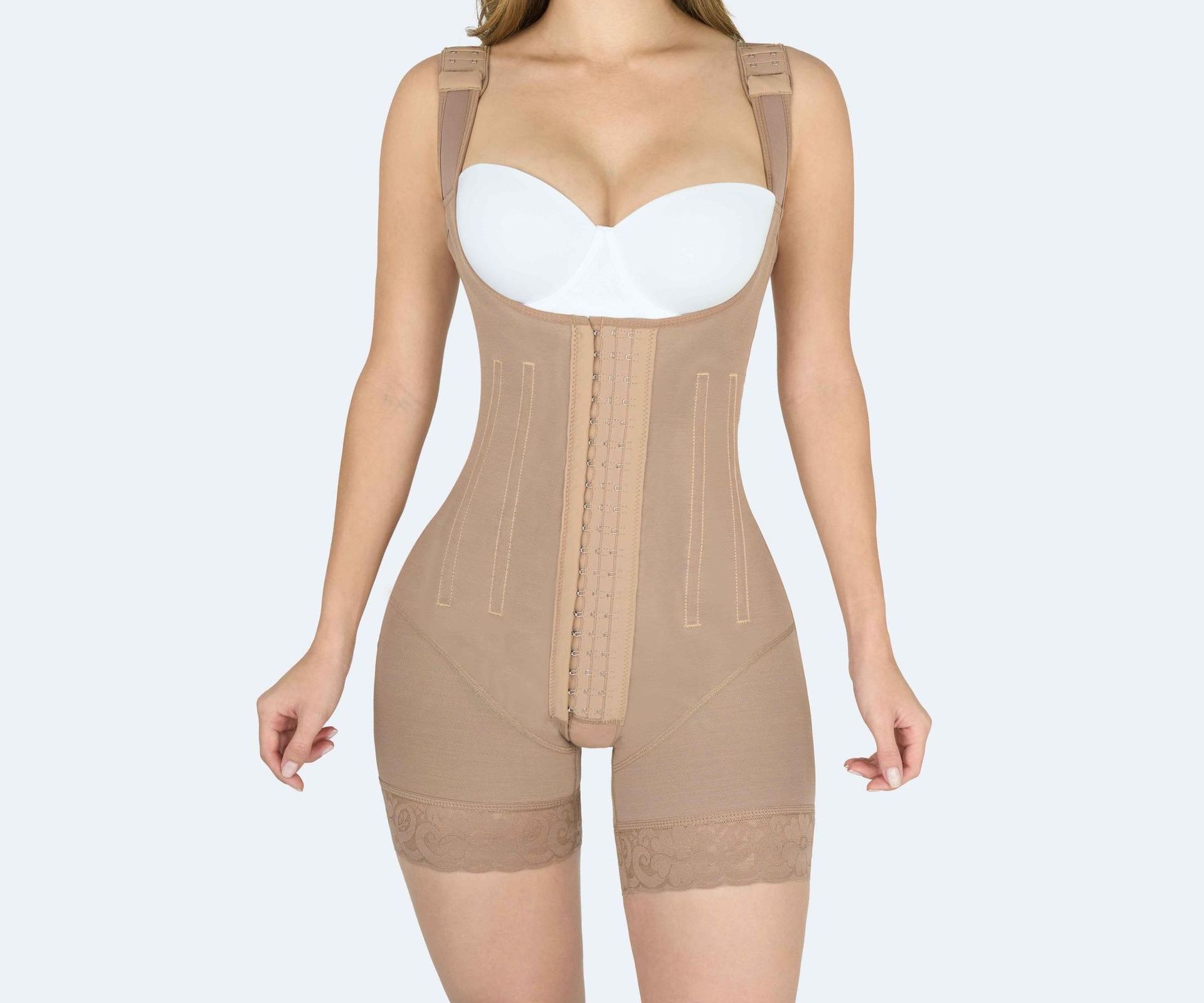 Tan full-body shapewear with attached straps and front closure, worn by a person.
