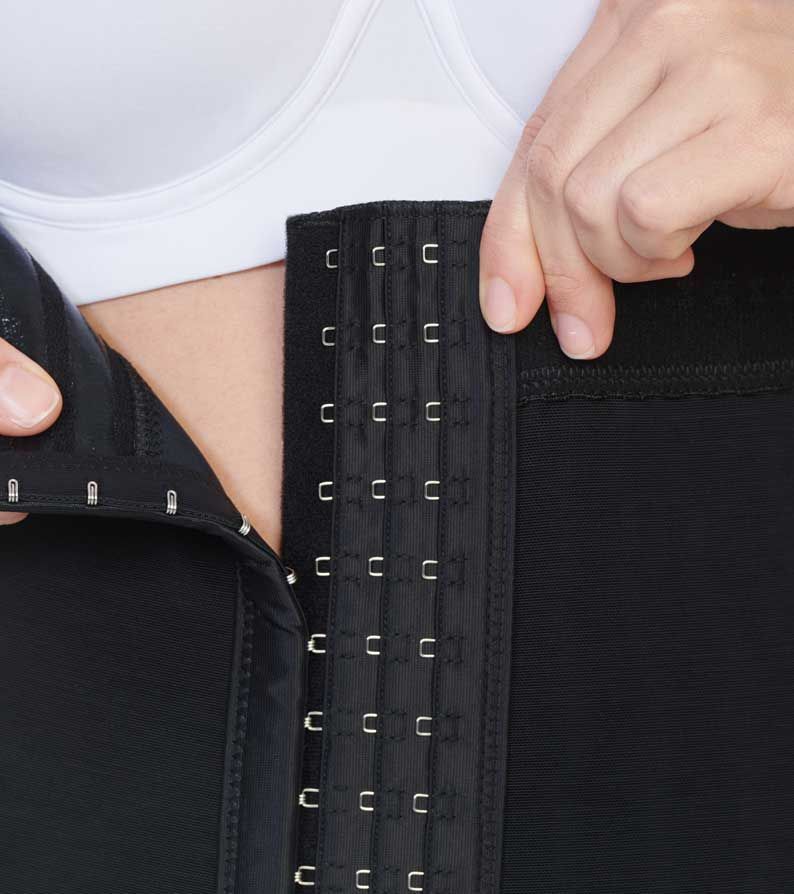 Person fastening a black waist cincher with metal hooks.