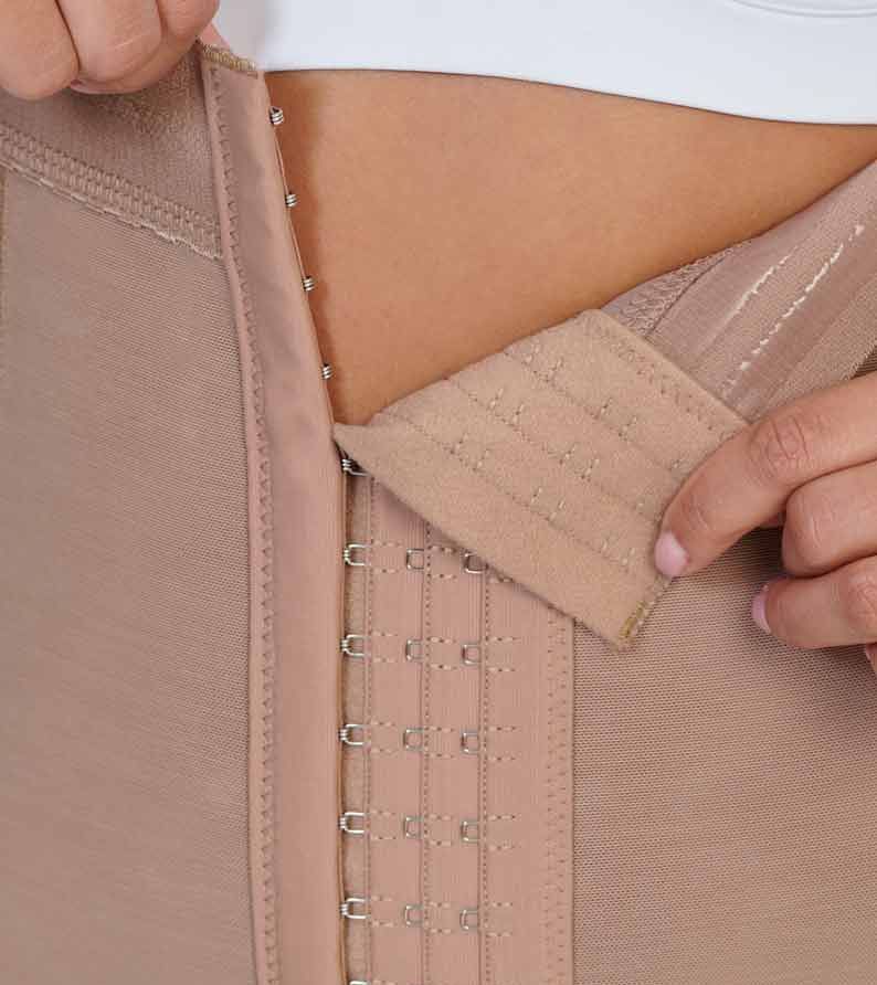 Person fastening a beige body shaper with hooks and eye closures on their abdomen.