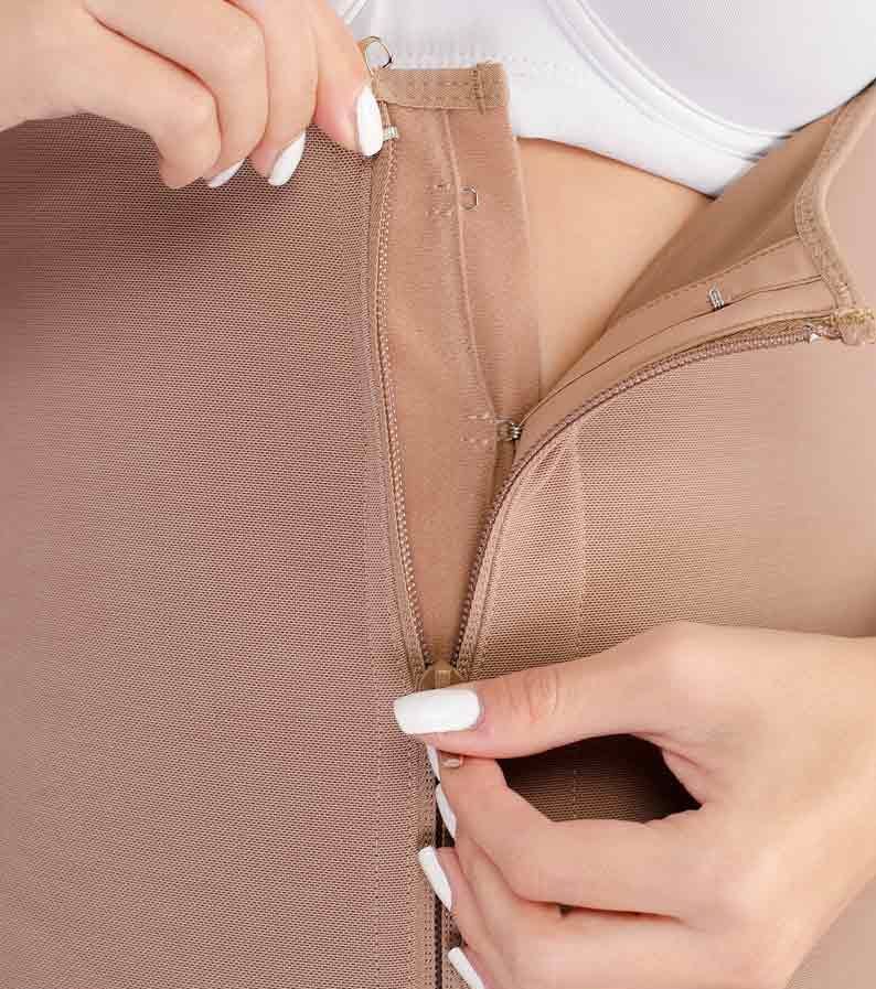 Person zipping up a beige compression garment. Hands, garment detail, white nails.