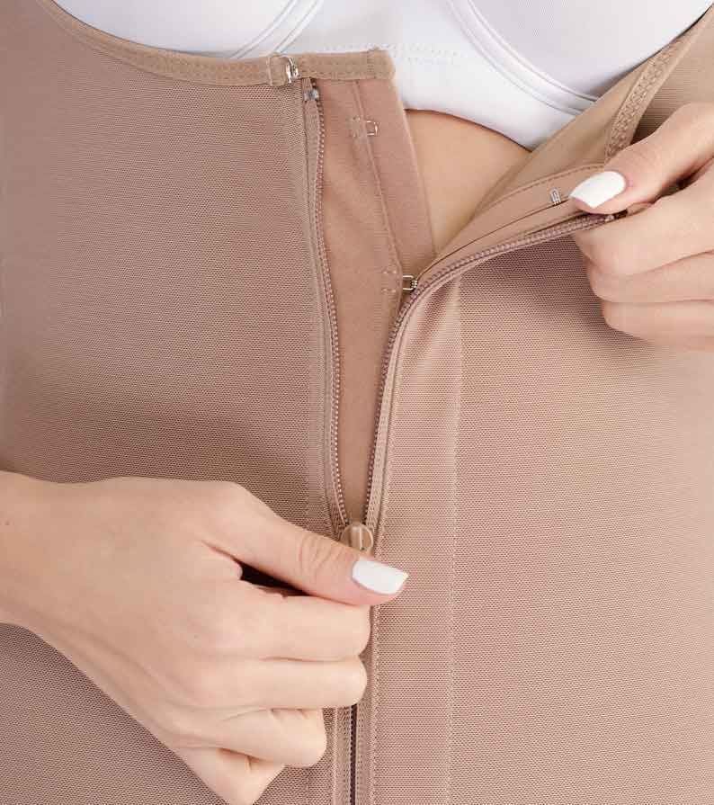 Woman zipping up a beige compression garment over a white bra.
