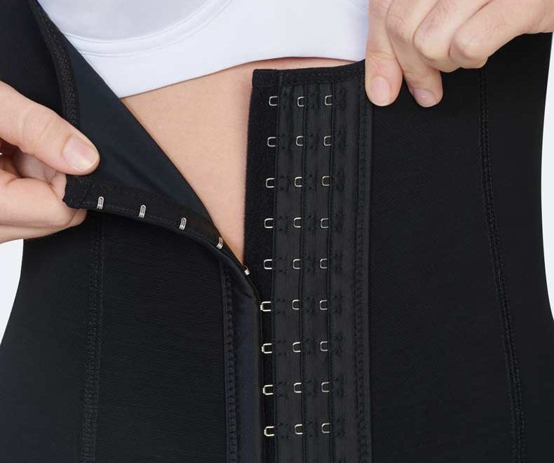 Hands fastening a black waist cincher with hooks.