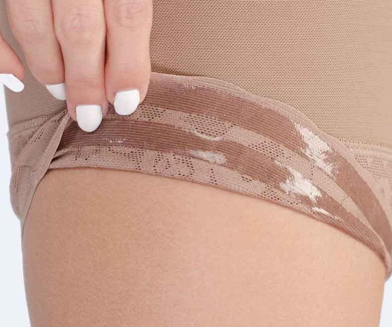 Close-up of a hand pulling up the waistband of tan shapewear.