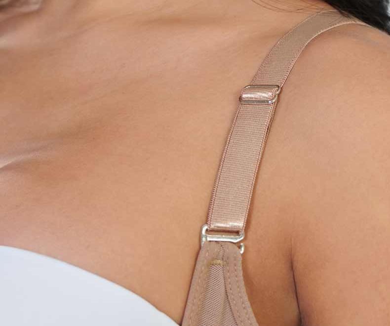 Close-up of a person's shoulder and bra strap, showing the strap's adjustment hardware. The strap is beige.