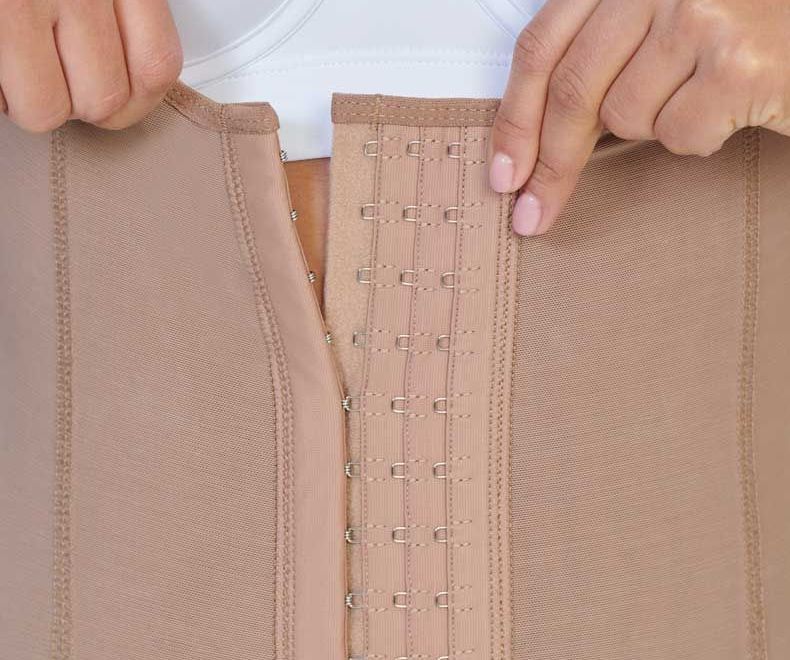 Person fastening a tan shapewear garment with hooks, close-up view.