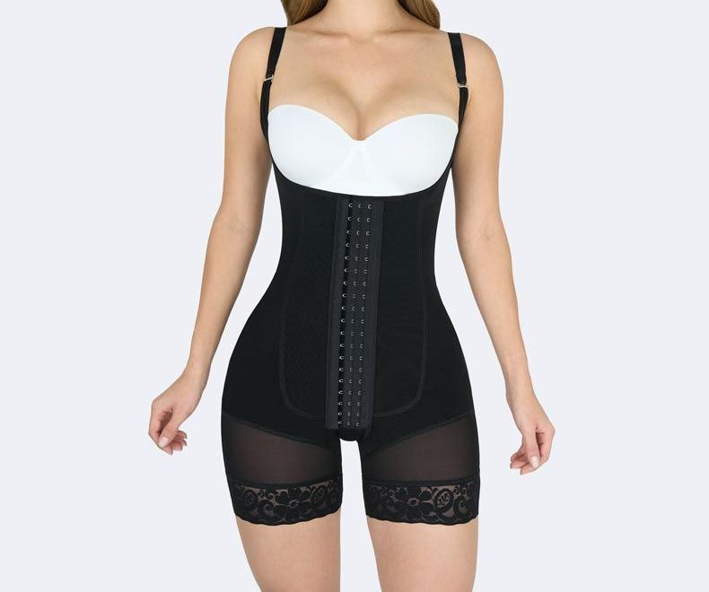 Woman wearing a black shapewear bodysuit with adjustable straps, hook closure, and lace-trimmed shorts.