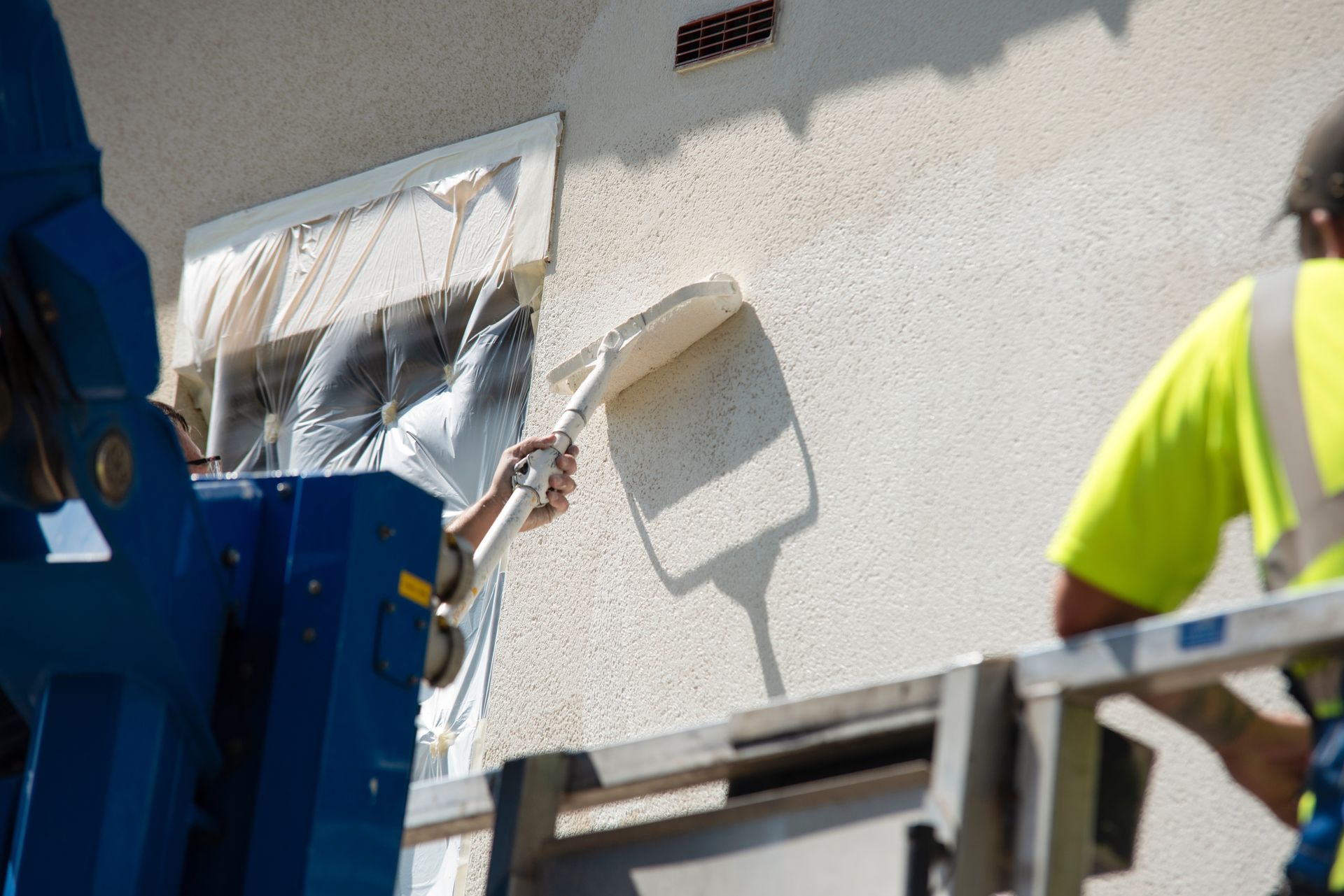 A man is painting the side of a building with a roller.