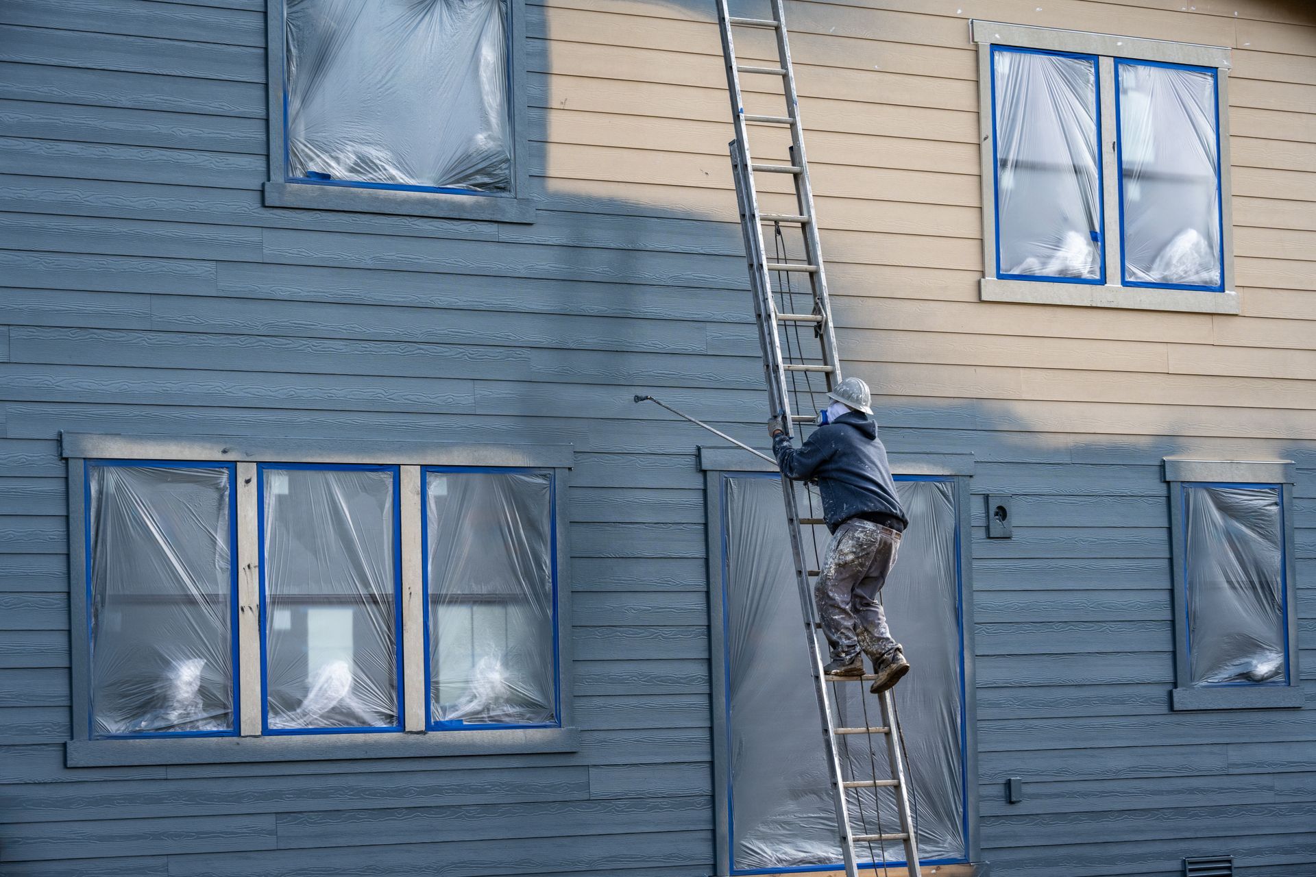 A man on a ladder is painting the side of a house.