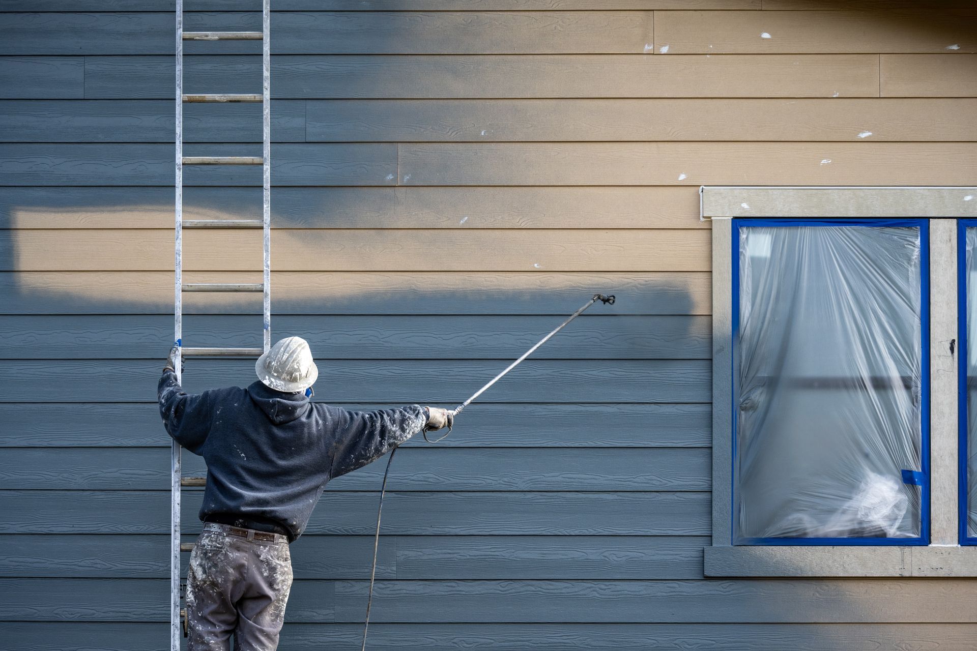 A man is standing on a ladder painting the side of a house.