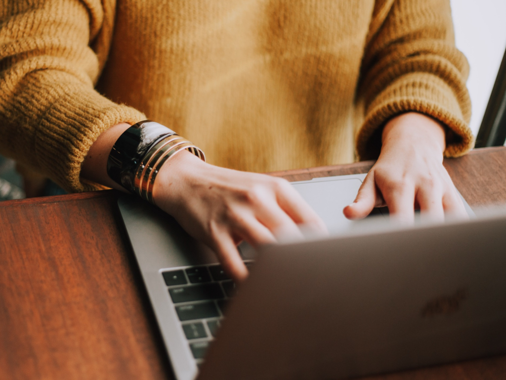 Uma mulher com um suéter amarelo está digitando em um laptop.