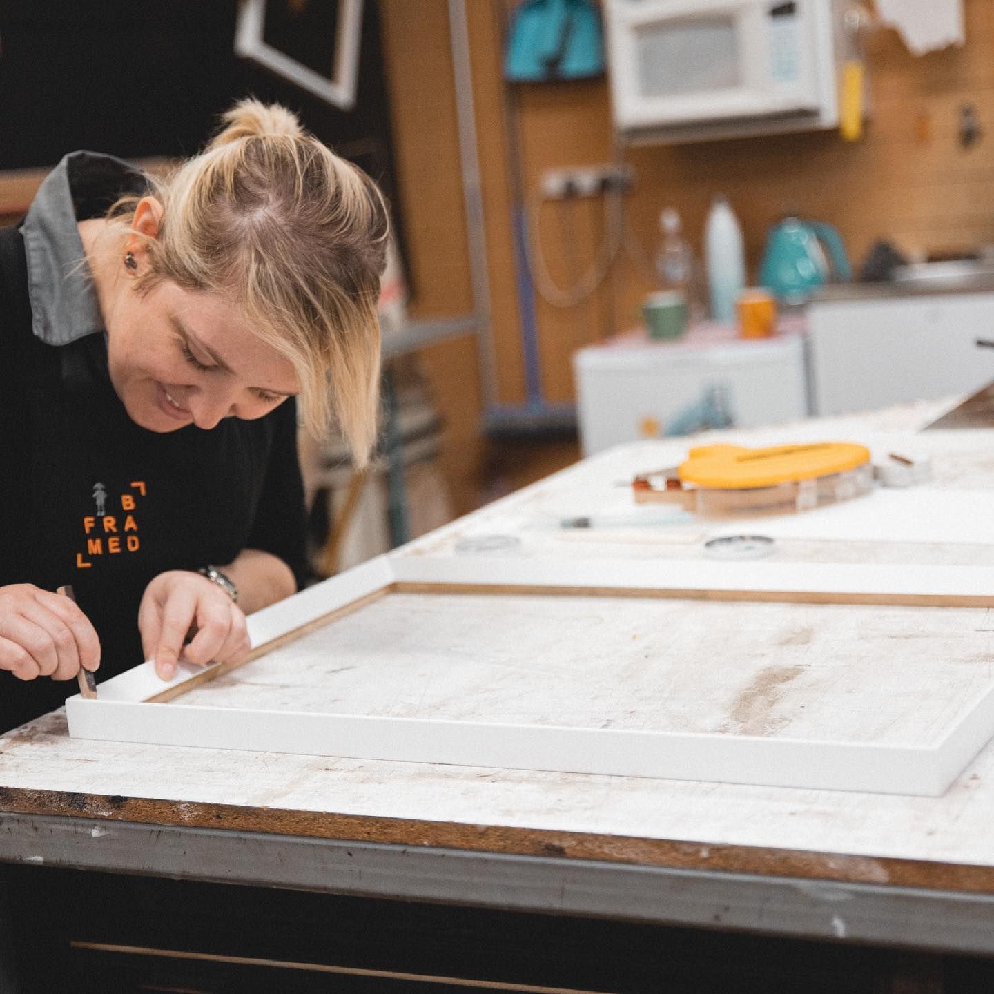A Woman Wearing a Black Shirt that Says B Framed Is Working on A Piece of Wood — B Framed Picture Framing in Ballina, NSW