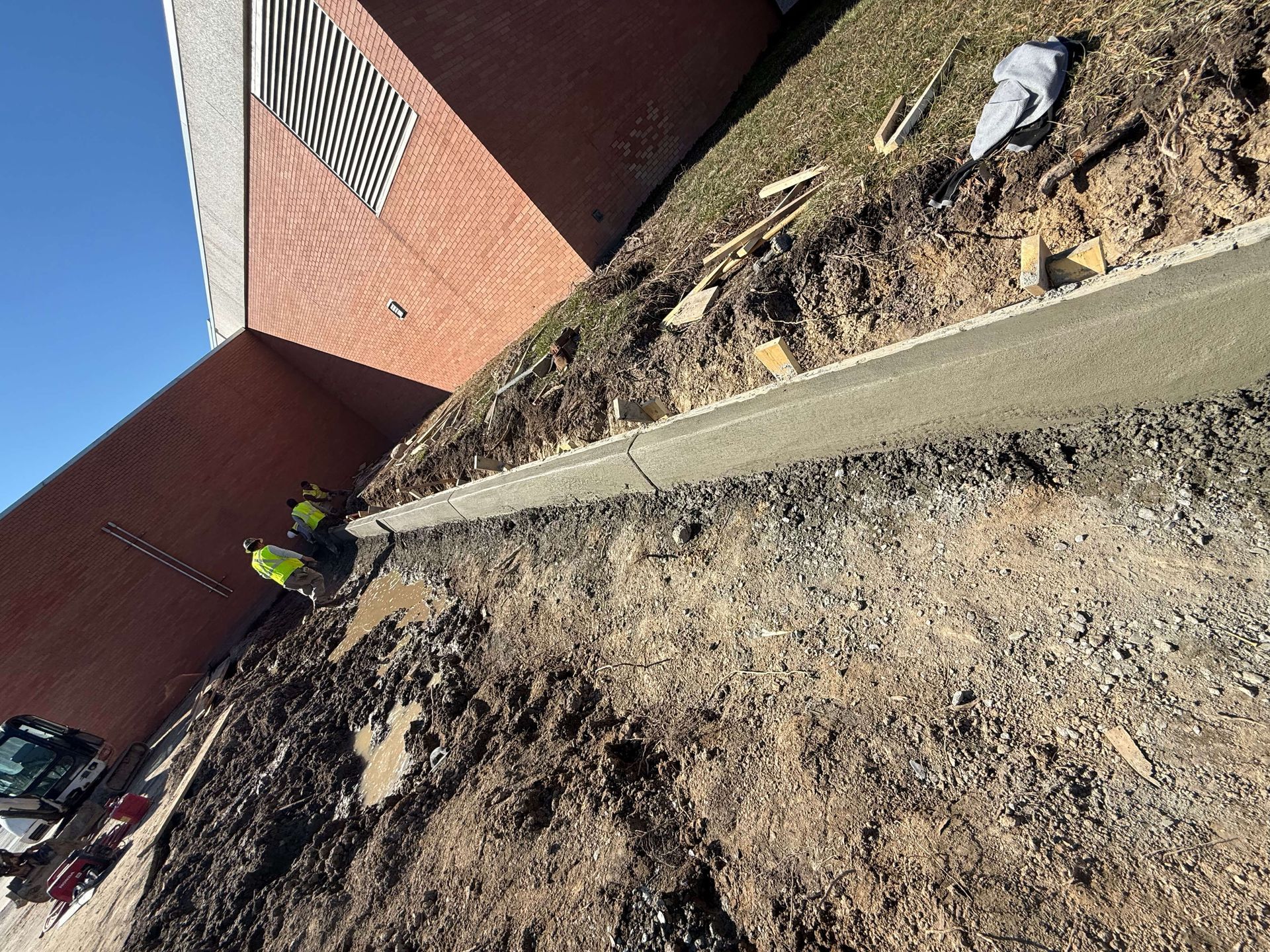 A group of construction workers are working on a sidewalk in front of a brick building.