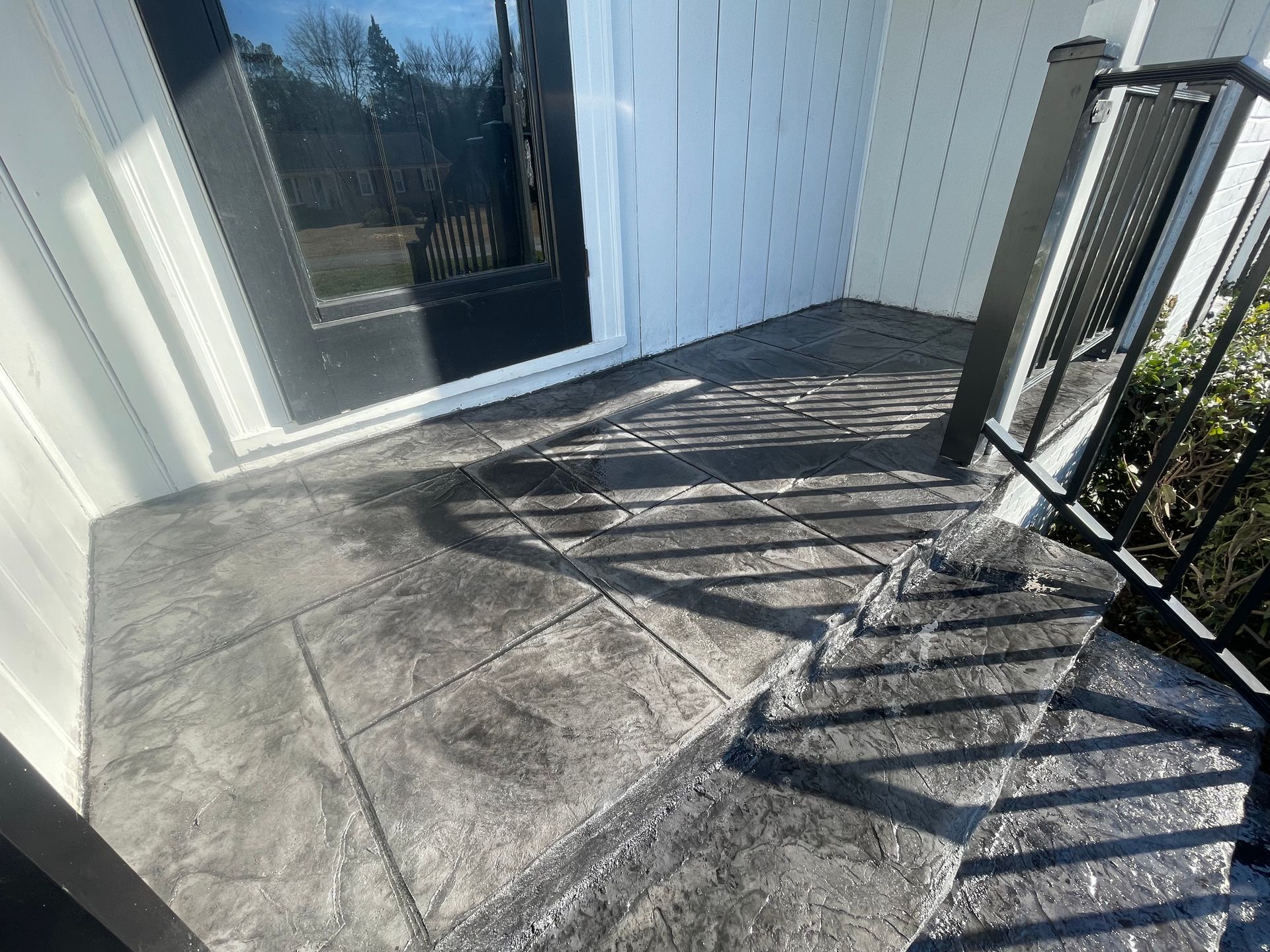 A concrete porch with a black railing and a black door.