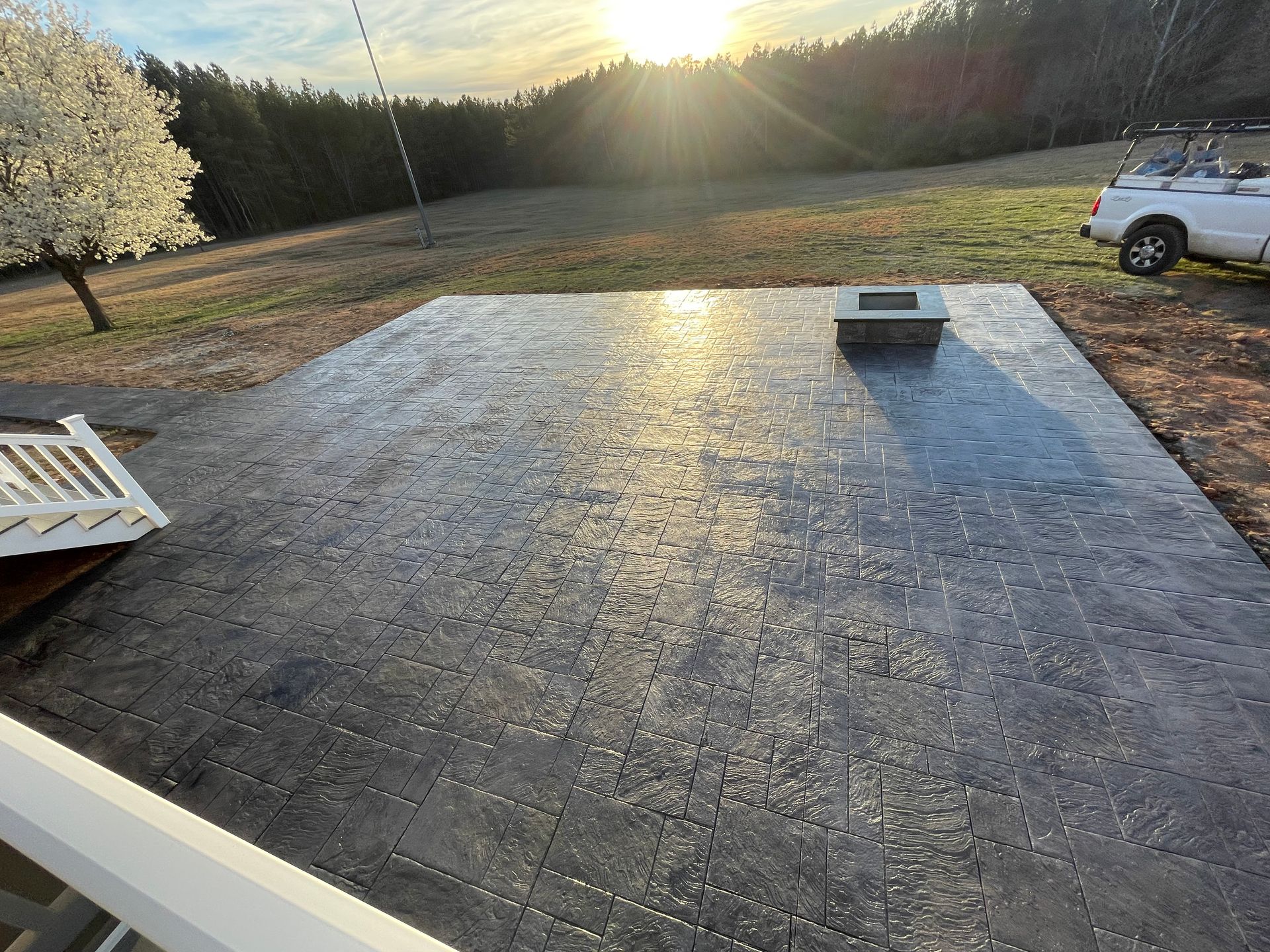 A concrete patio with a fire pit and a white truck parked in the background.