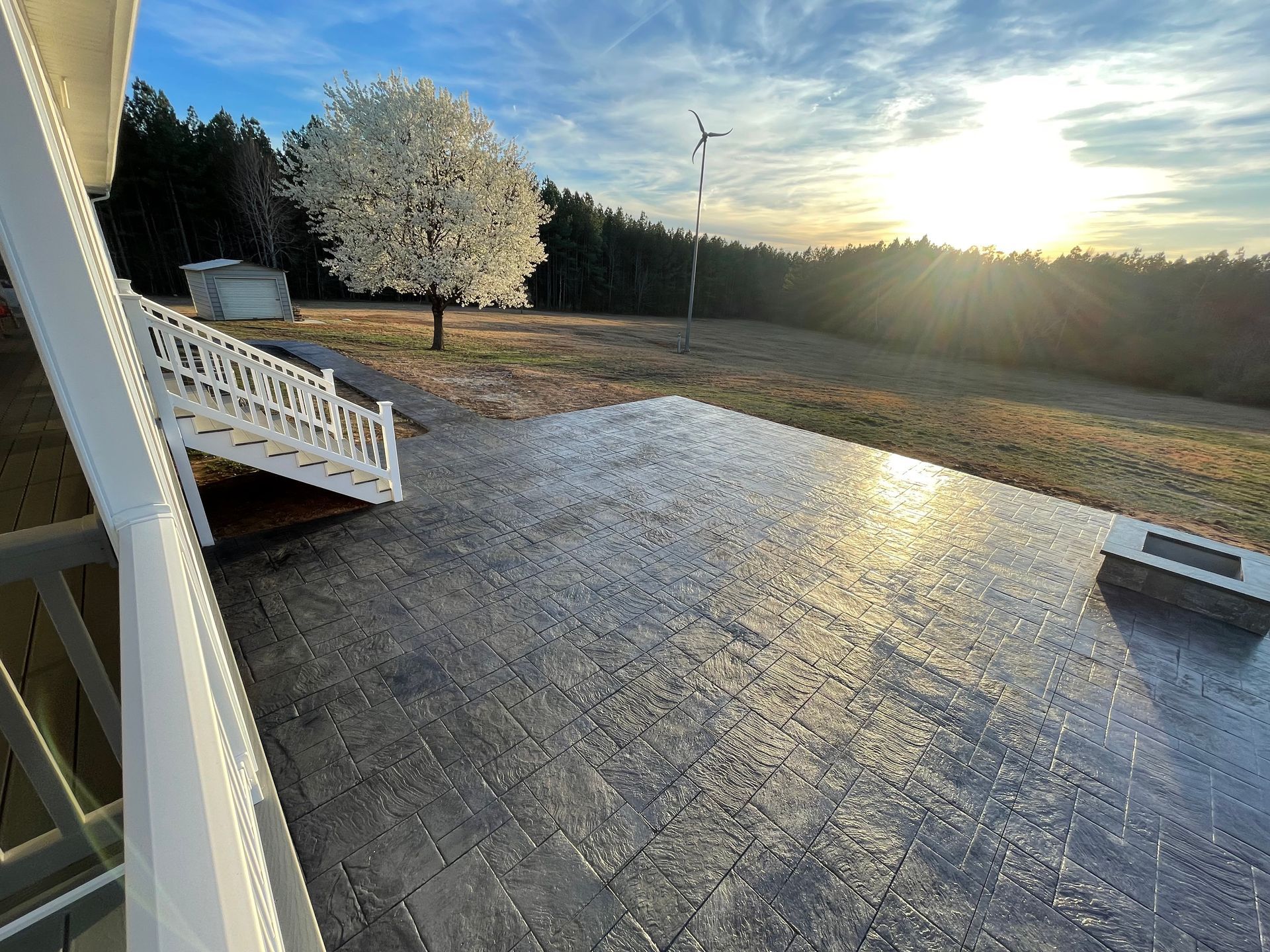 A patio with a tree in the background and the sun shining through the clouds.