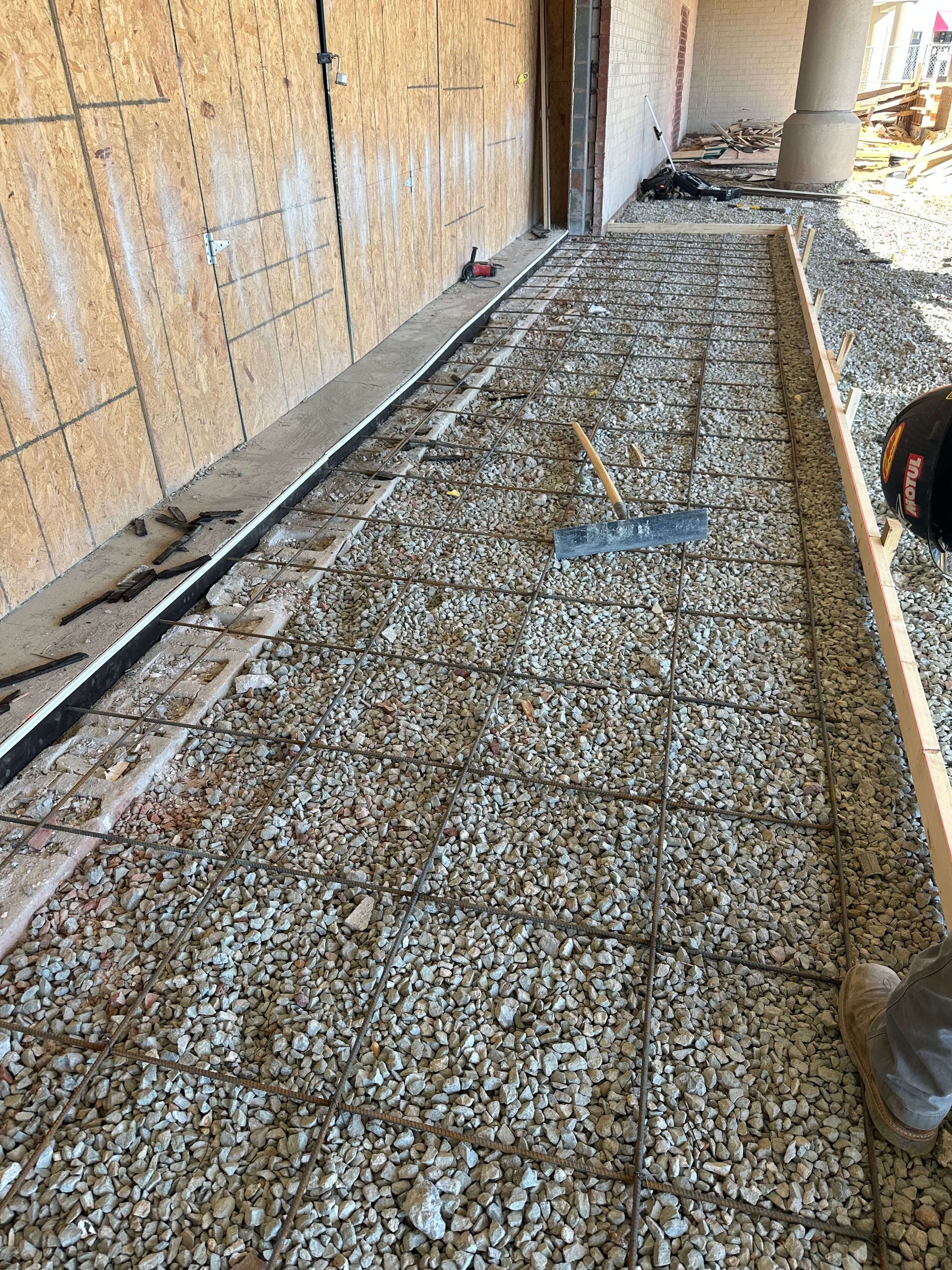 A person is laying gravel on the ground in front of a building.