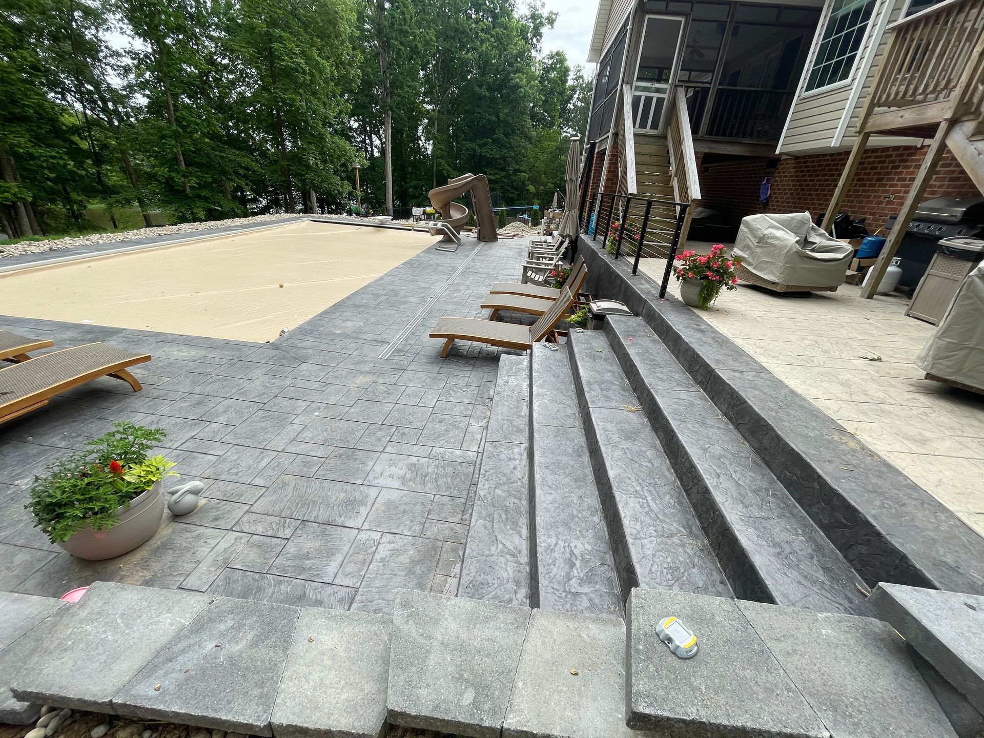 A patio with stairs leading up to a pool and a house in the background.