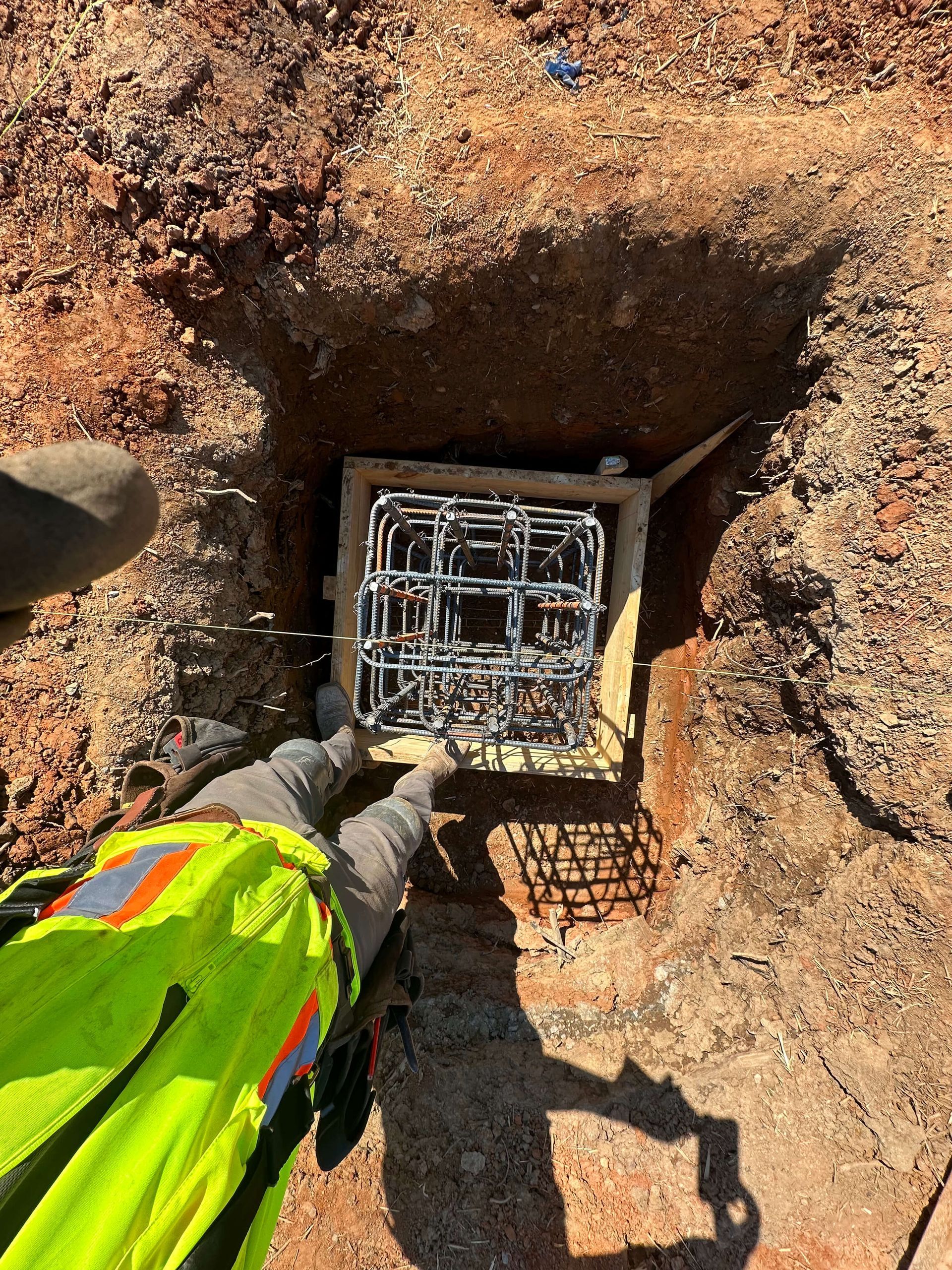 A person in a yellow vest is holding a box in the dirt.