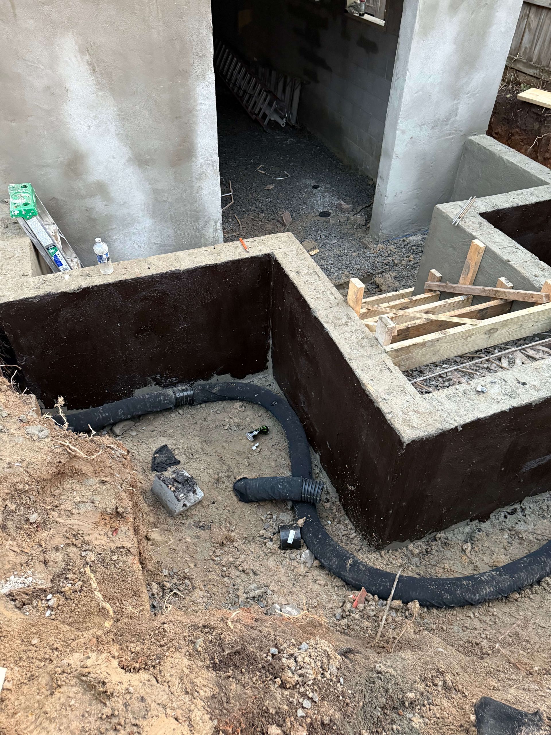 A hose is laying in the dirt next to a concrete wall.