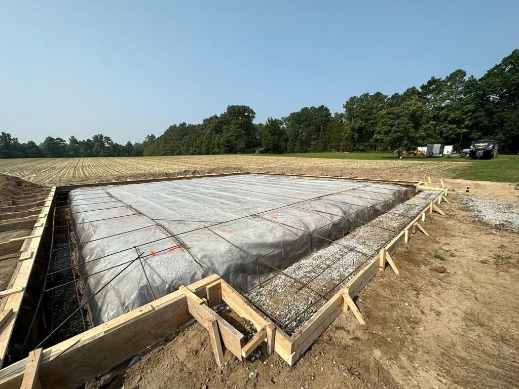 A concrete foundation is being built in a field with trees in the background.