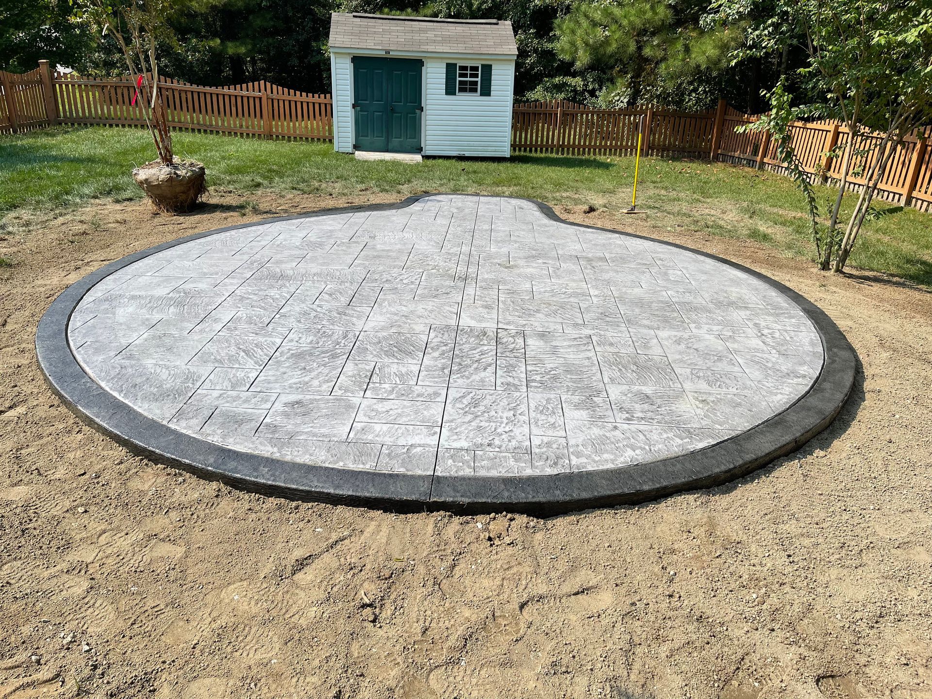 A circular patio in a backyard with a shed in the background.