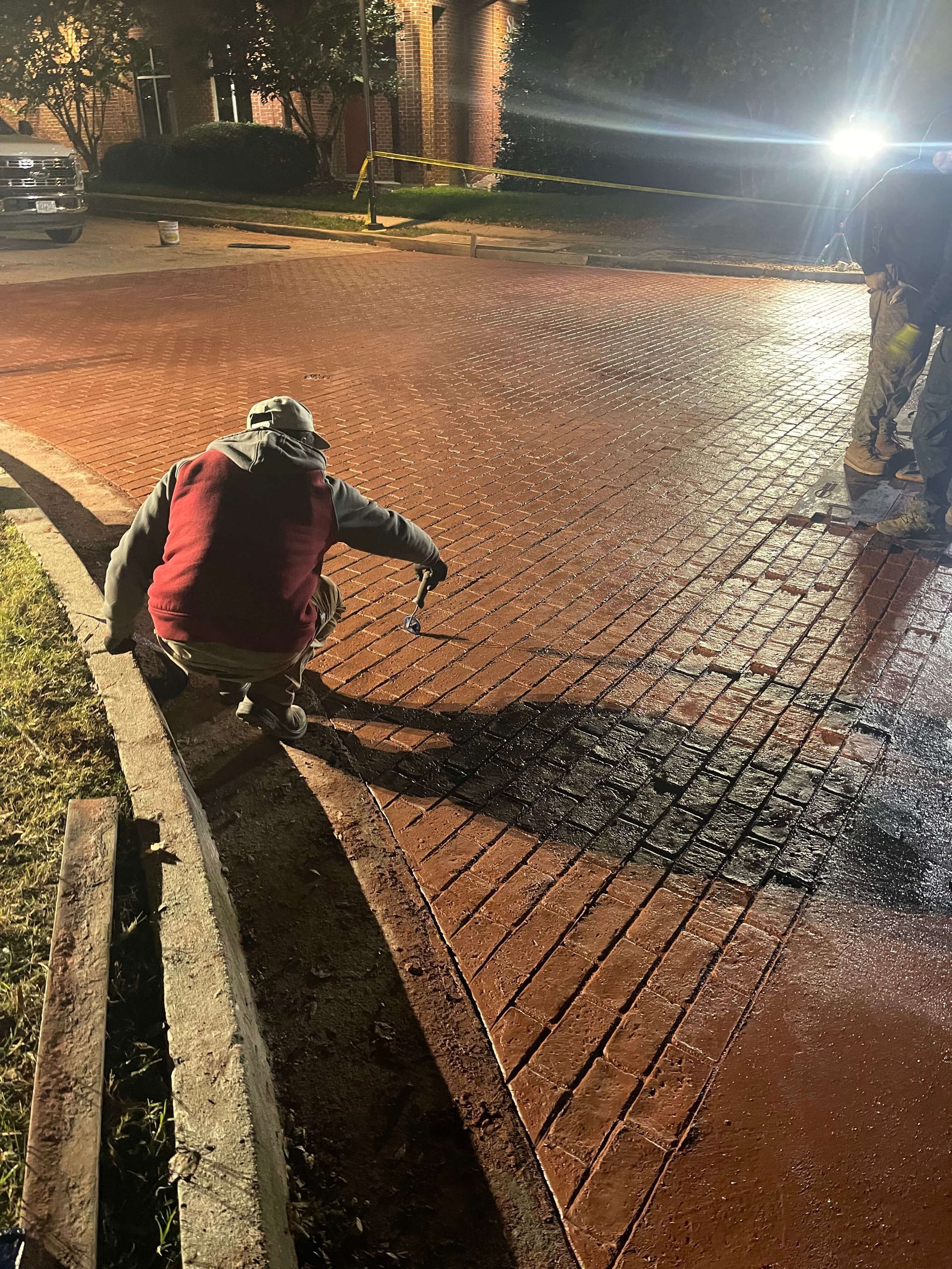 A man is working on a brick driveway at night.