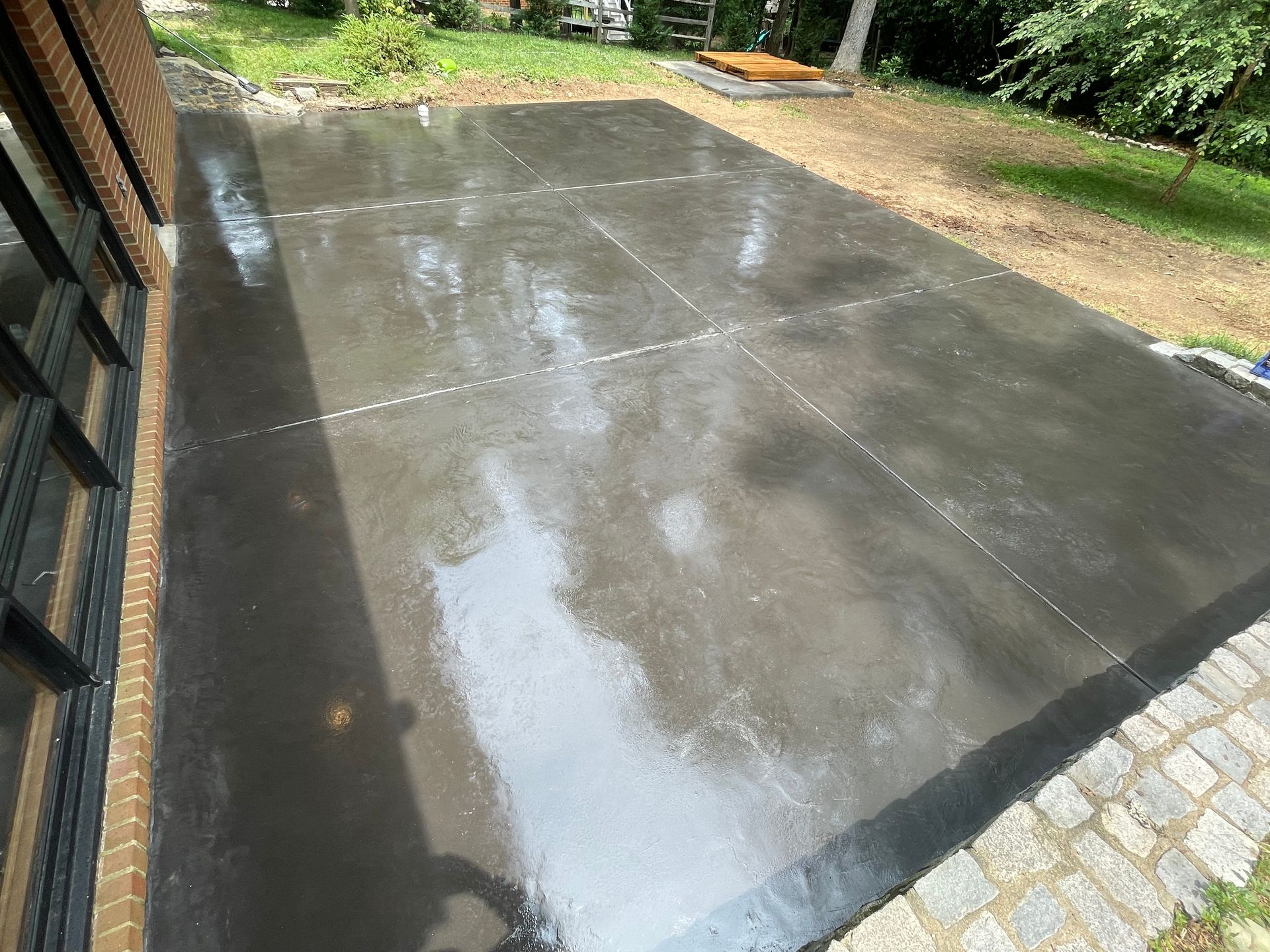 A large concrete patio with a brick border is being built in a backyard.