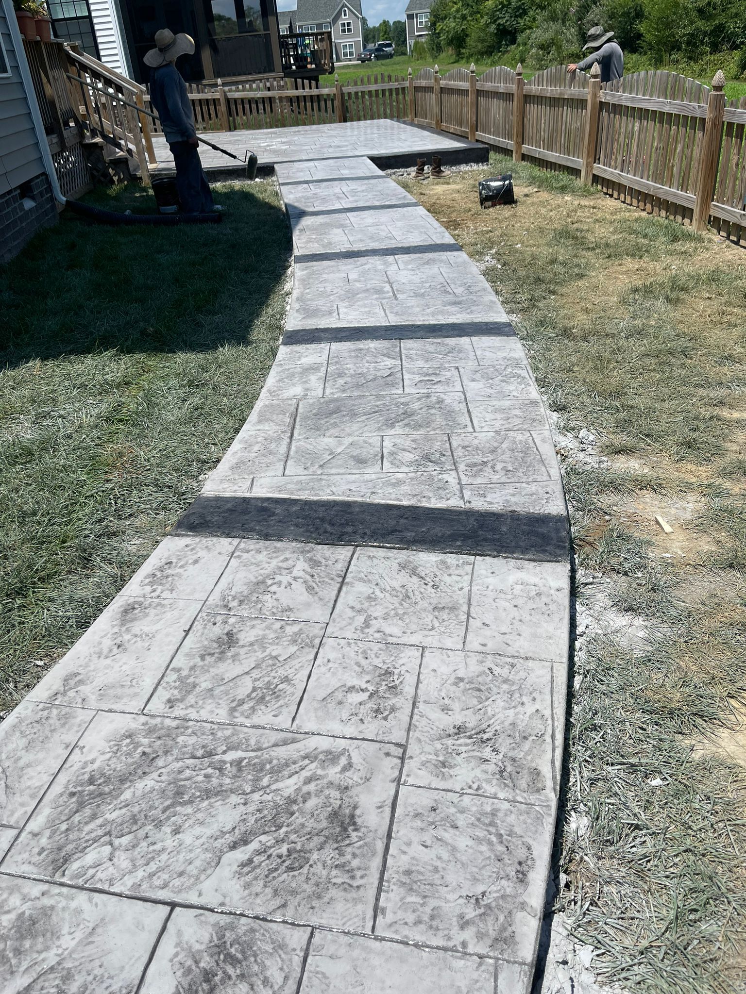 A man is standing on a concrete walkway next to a wooden fence.