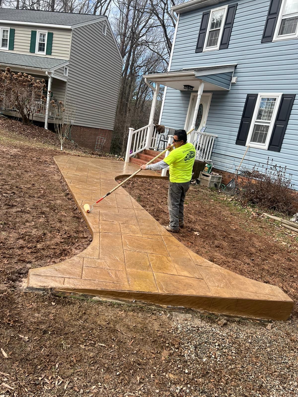 A man is painting a sidewalk in front of a house.