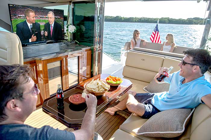 Two men are sitting on a boat watching a television.