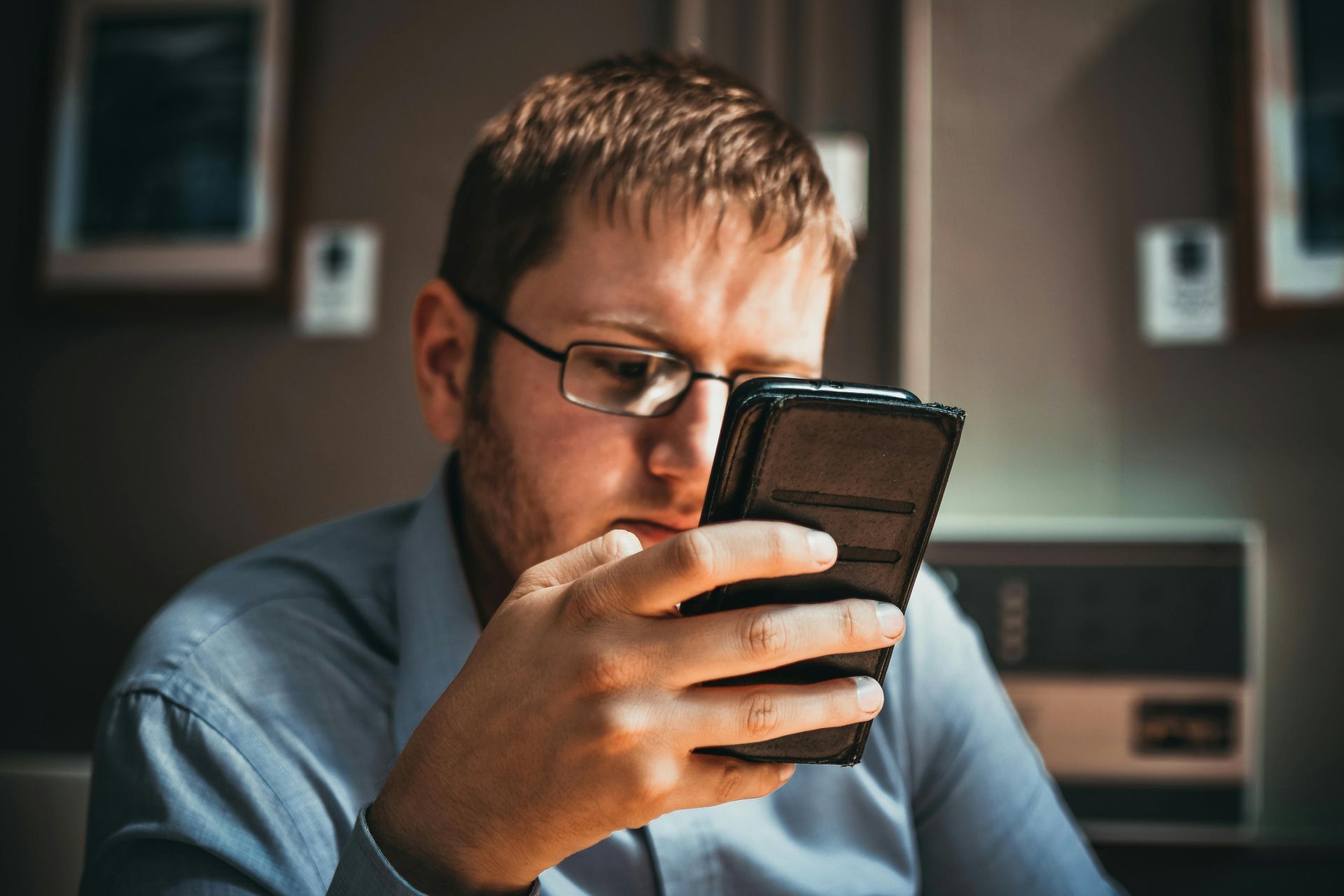 Um homem usando óculos está olhando para seu celular.