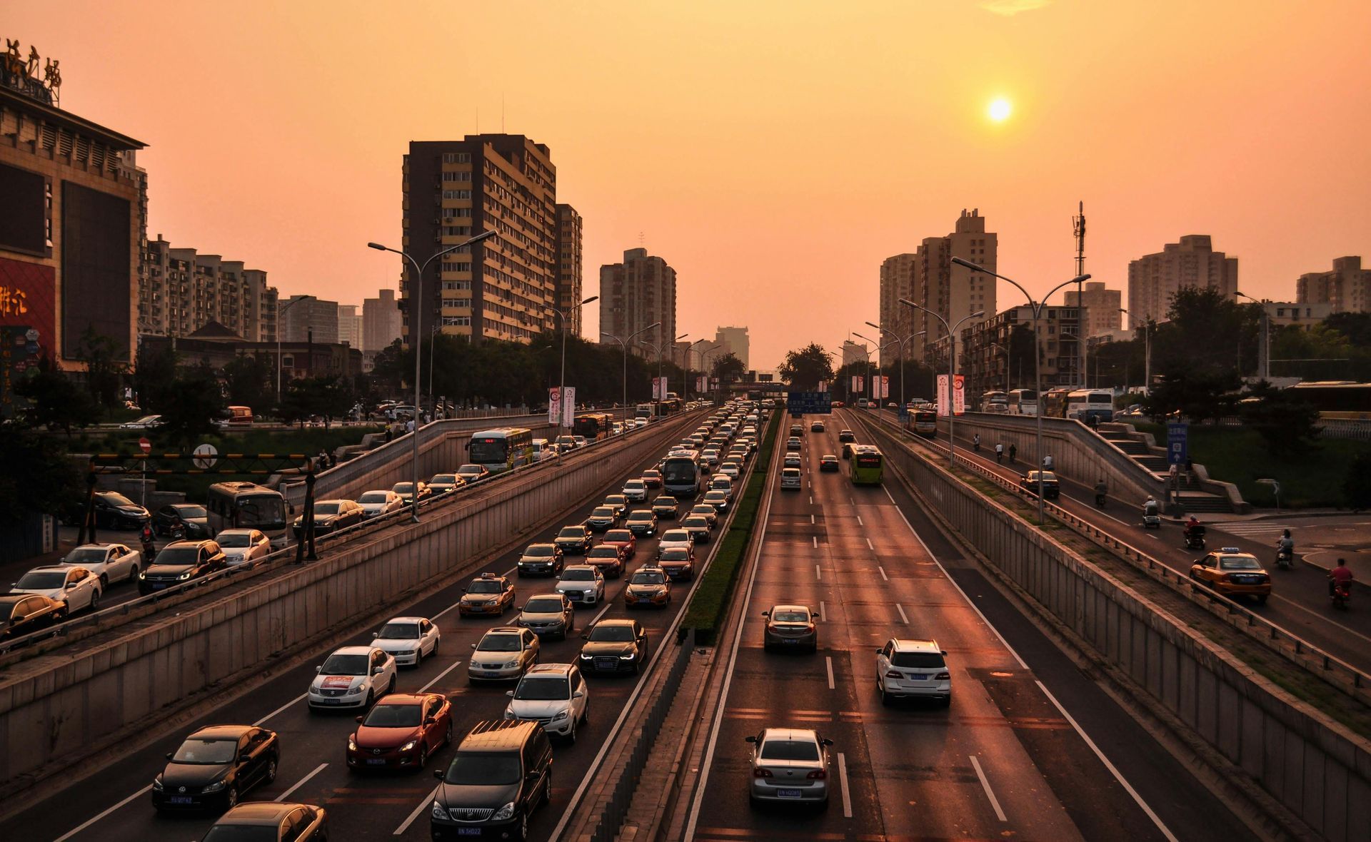 Cars on a highway in a city at sunset, orange sky, tall buildings in the background.