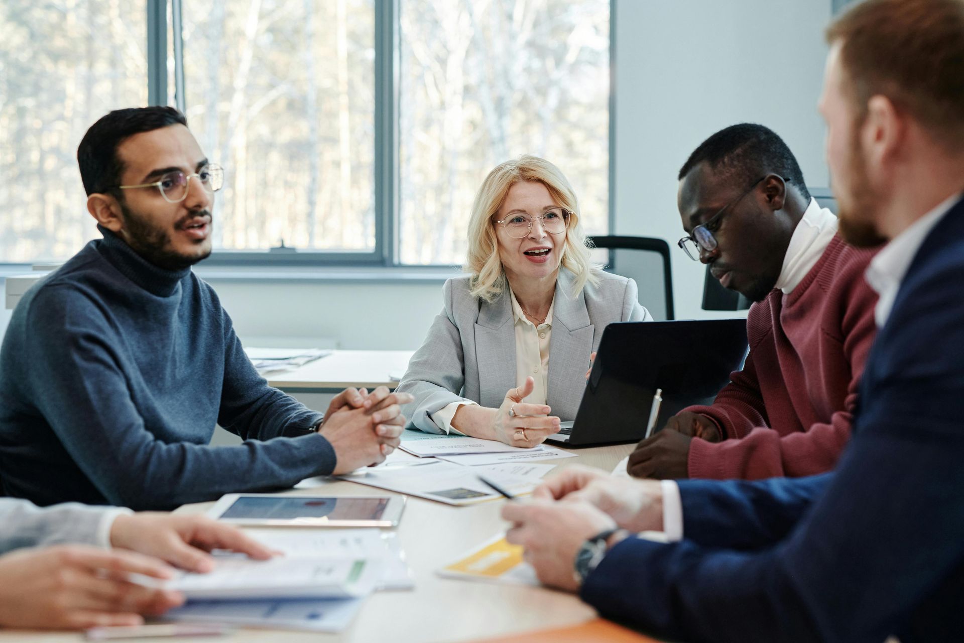 Business meeting at a table: People are discussing documents and a laptop, in a bright office.