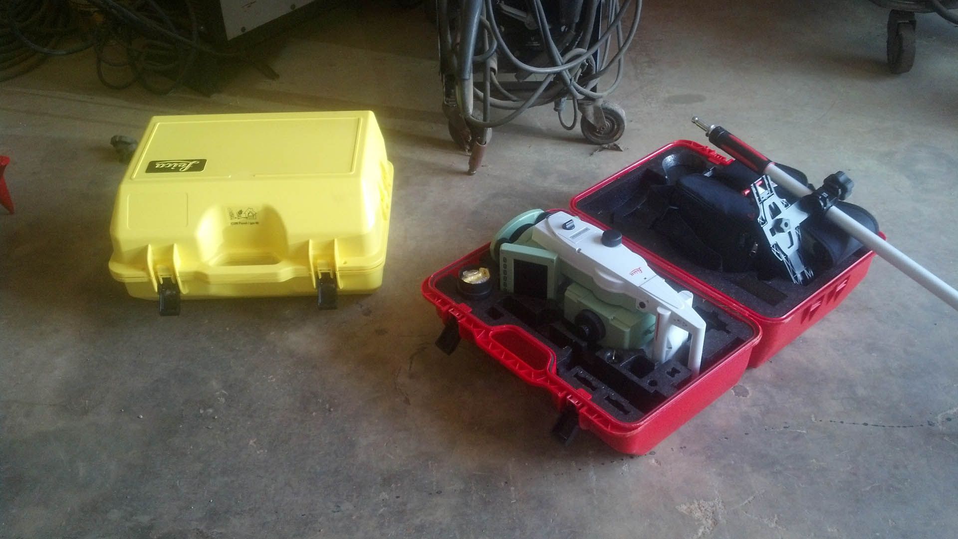 Yellow and red cases on concrete floor; one open with surveying equipment inside.