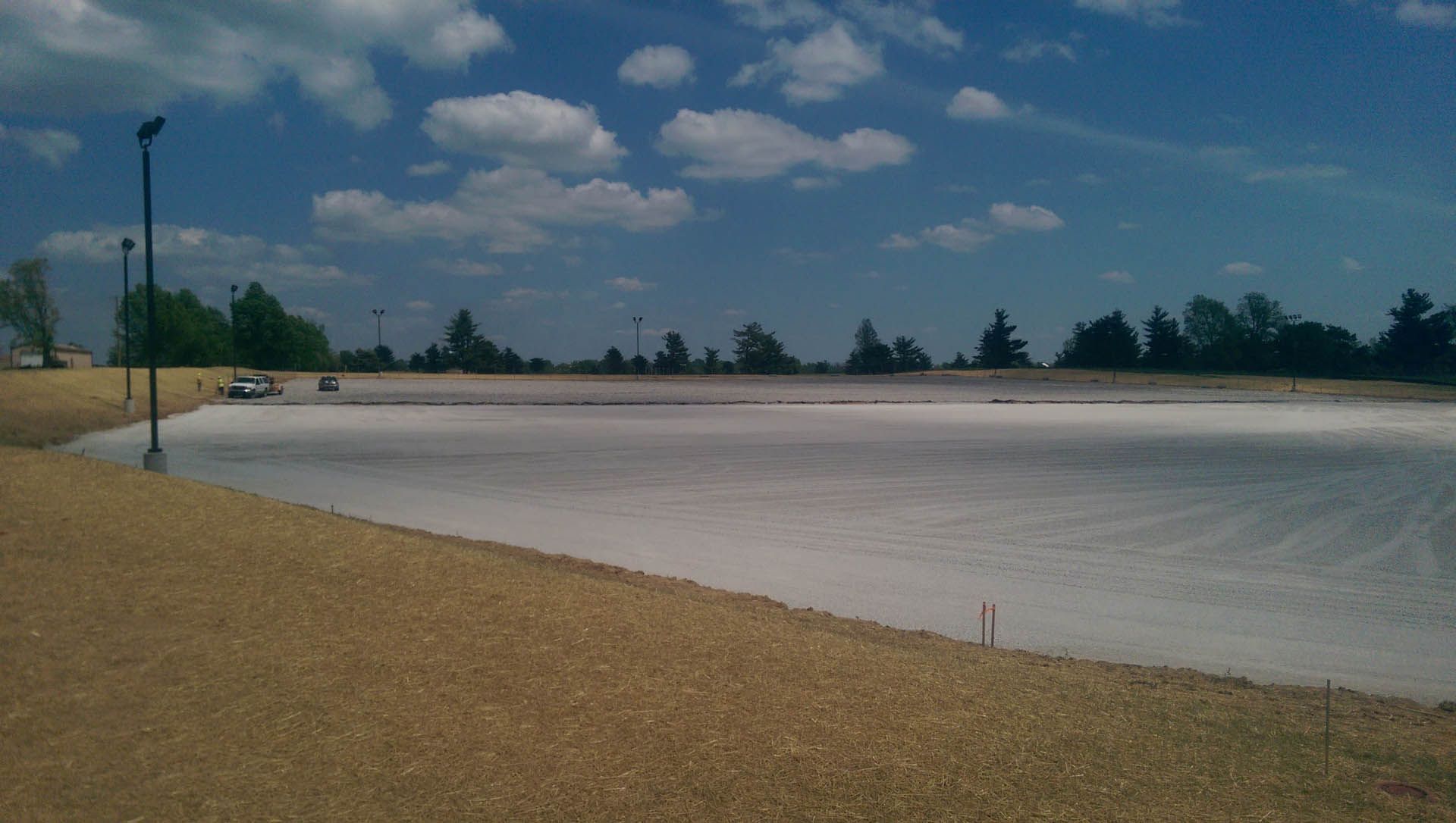 Large, light-colored pond surrounded by tan earth under a blue sky with scattered clouds.